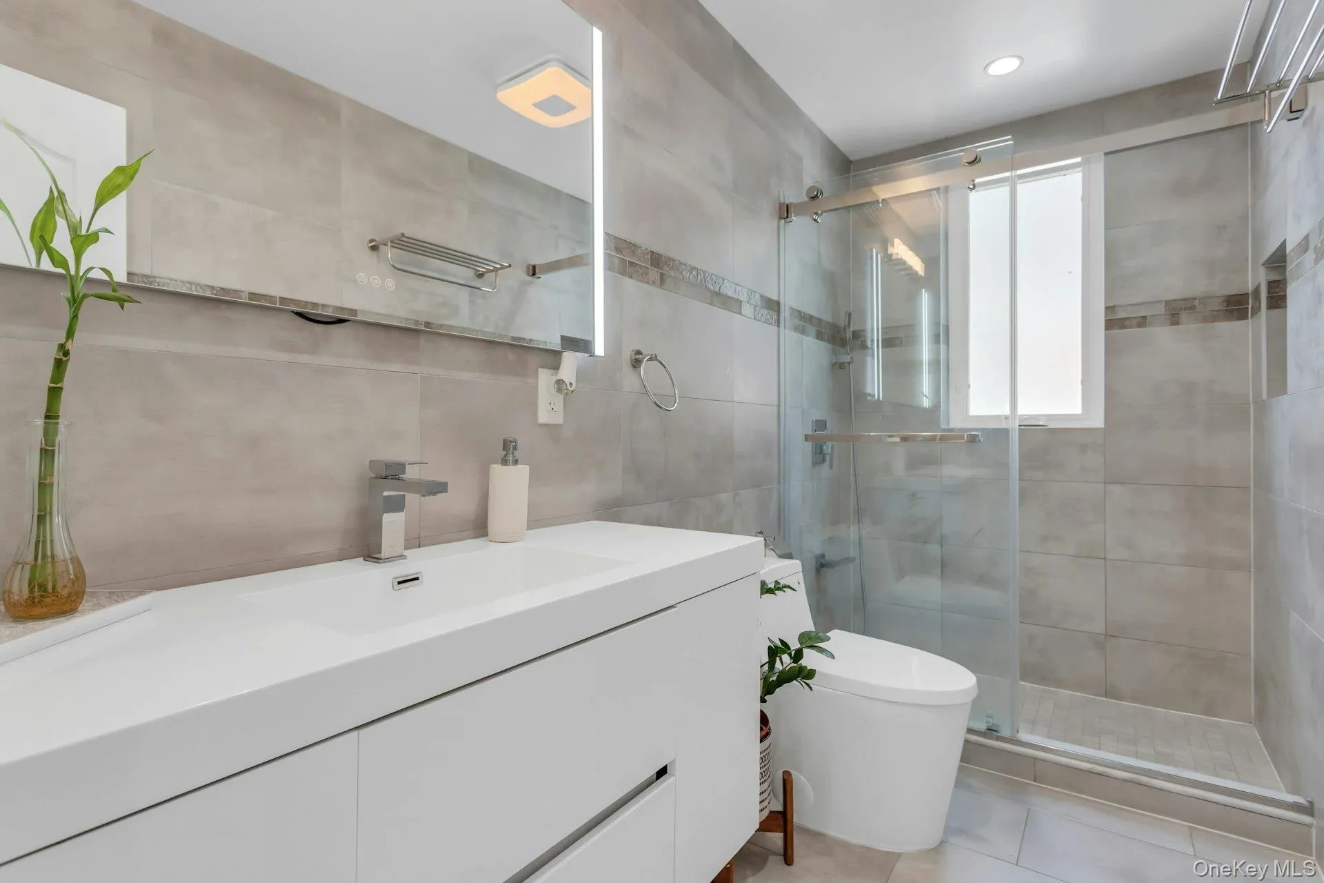 Contemporary bathroom featuring a floating white vanity with integrated sink, chrome faucet, and an illuminated mirror Contemporary bathroom featuring a floating white vanity with integrated sink, chrome faucet, and an illuminated mirror