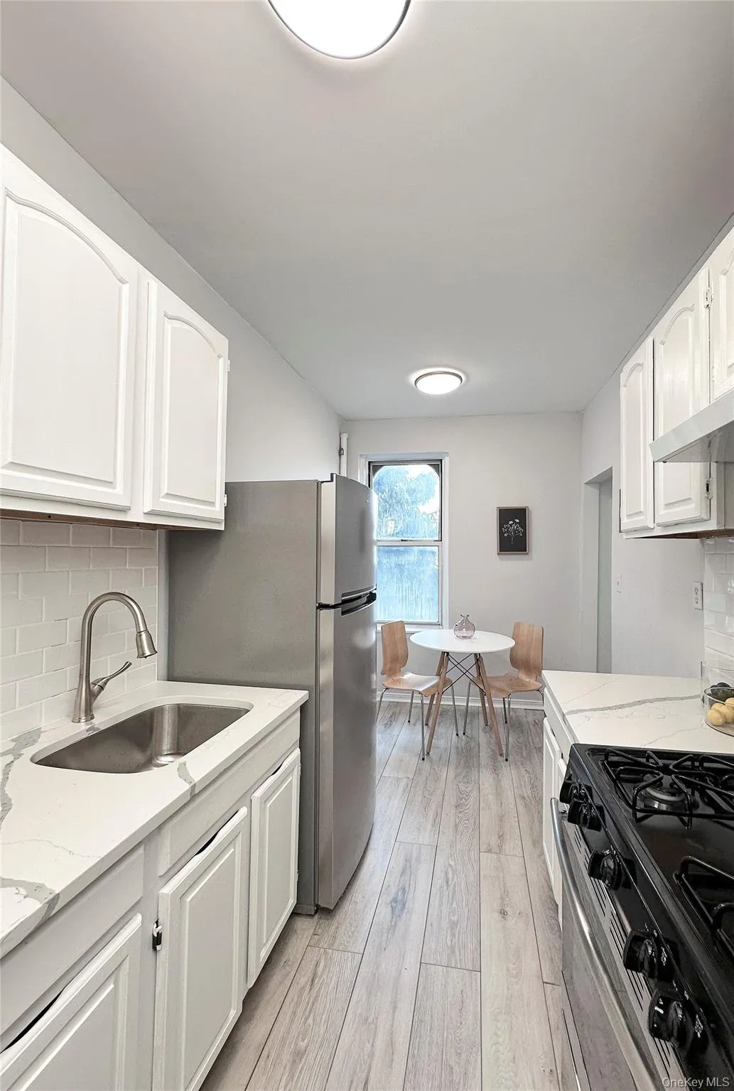 Eat in kitchen featuring white cabinetry, light-toned wood-finish flooring, and a subway tile backsplash Eat in kitchen featuring white cabinetry, light-toned wood-finish flooring, and a subway tile backsplash