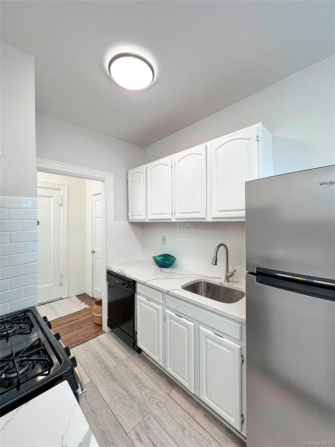 Kitchen featuring white shaker-style cabinetry, a white subway tile backsplash, and a stainless steel refrigerator Kitchen featuring white shaker-style cabinetry, a white subway tile backsplash, and a stainless steel refrigerator