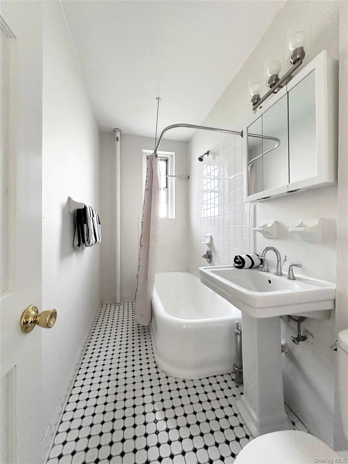 Bathroom featuring a white pedestal sink, a classic white bathtub, black and white mosaic tile flooring, a mirrored medicine cabinet, and a window with privacy glass and freshly reglazed soaking tub. Bathroom featuring a white pedestal sink, a classic white bathtub, black and white mosaic tile flooring, a mirrored medicine cabinet, and a window with privacy glass and freshly reglazed soaking tub.