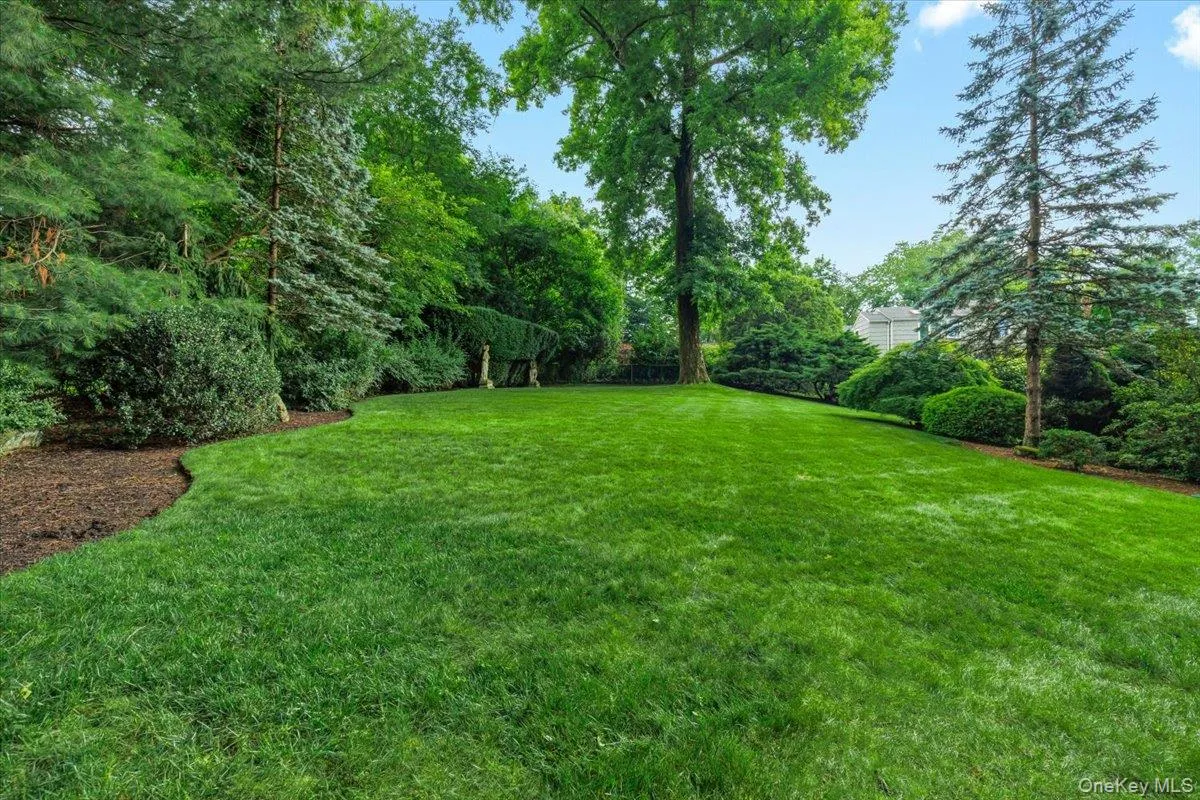 Spacious lawn bordered by mature trees and shrubs, featuring a mulched edge, an established tree, and verdant landscaping Spacious lawn bordered by mature trees and shrubs, featuring a mulched edge, an established tree, and verdant landscaping