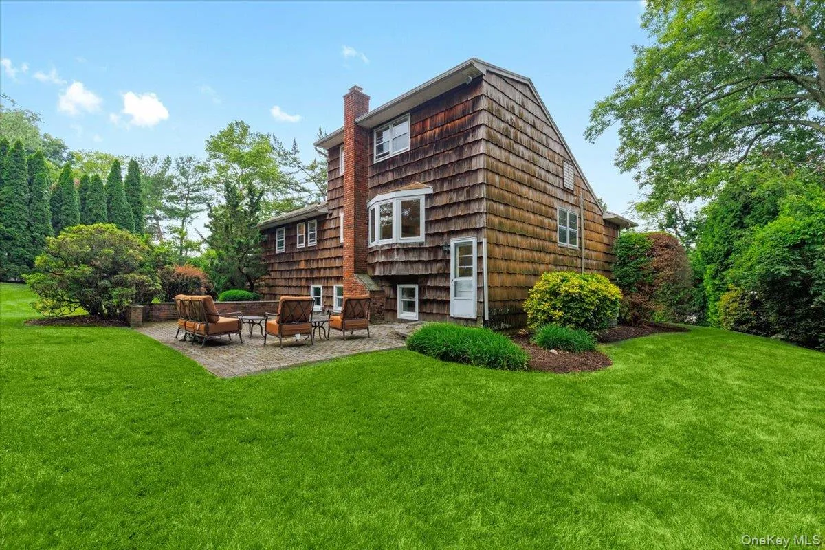 Rear exterior featuring a spacious lawn, brick chimney, bay window, natural wood shake siding, and a patio Rear exterior featuring a spacious lawn, brick chimney, bay window, natural wood shake siding, and a patio