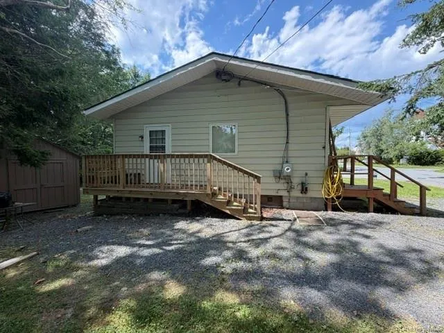 Exterior featuring light-colored siding, a dark shingled roof, a wooden deck, and a detached storage shed Exterior featuring light-colored siding, a dark shingled roof, a wooden deck, and a detached storage shed