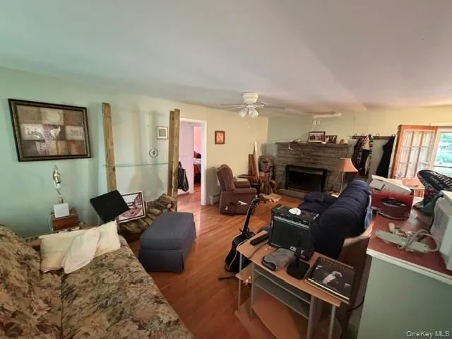 Wood-finish flooring throughout, stone fireplace with dark insert, white ceiling fan, and light wall paint Wood-finish flooring throughout, stone fireplace with dark insert, white ceiling fan, and light wall paint