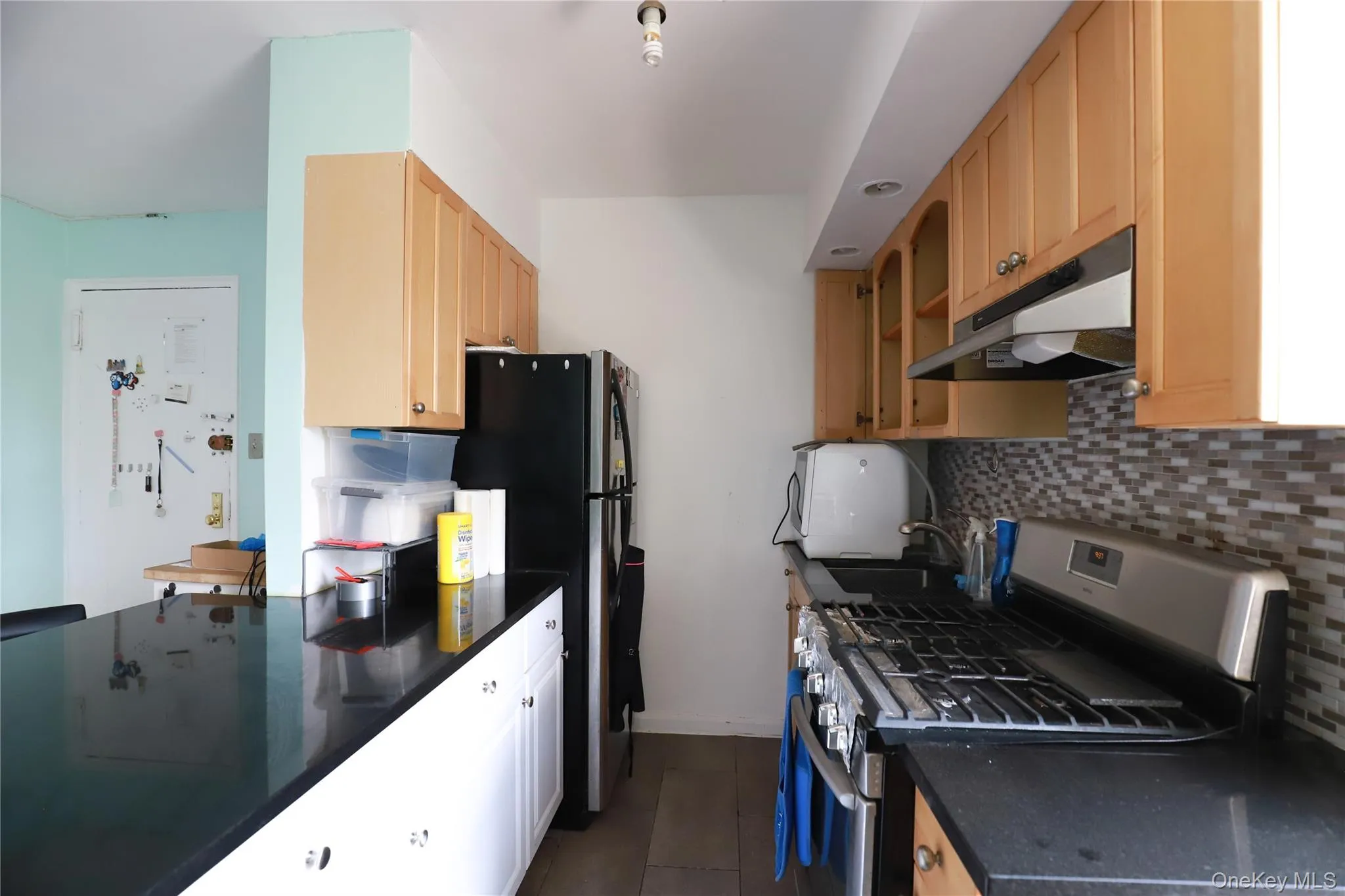 Kitchen featuring wood-finish cabinetry, black countertops, stainless steel appliances, and a tiled backsplash Kitchen featuring wood-finish cabinetry, black countertops, stainless steel appliances, and a tiled backsplash