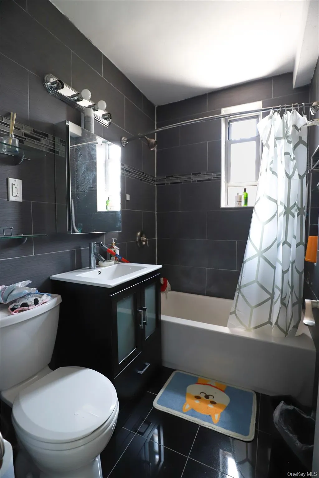 Bathroom featuring dark tiled walls and floors, a white vanity sink, and a built-in bathtub with shower Bathroom featuring dark tiled walls and floors, a white vanity sink, and a built-in bathtub with shower