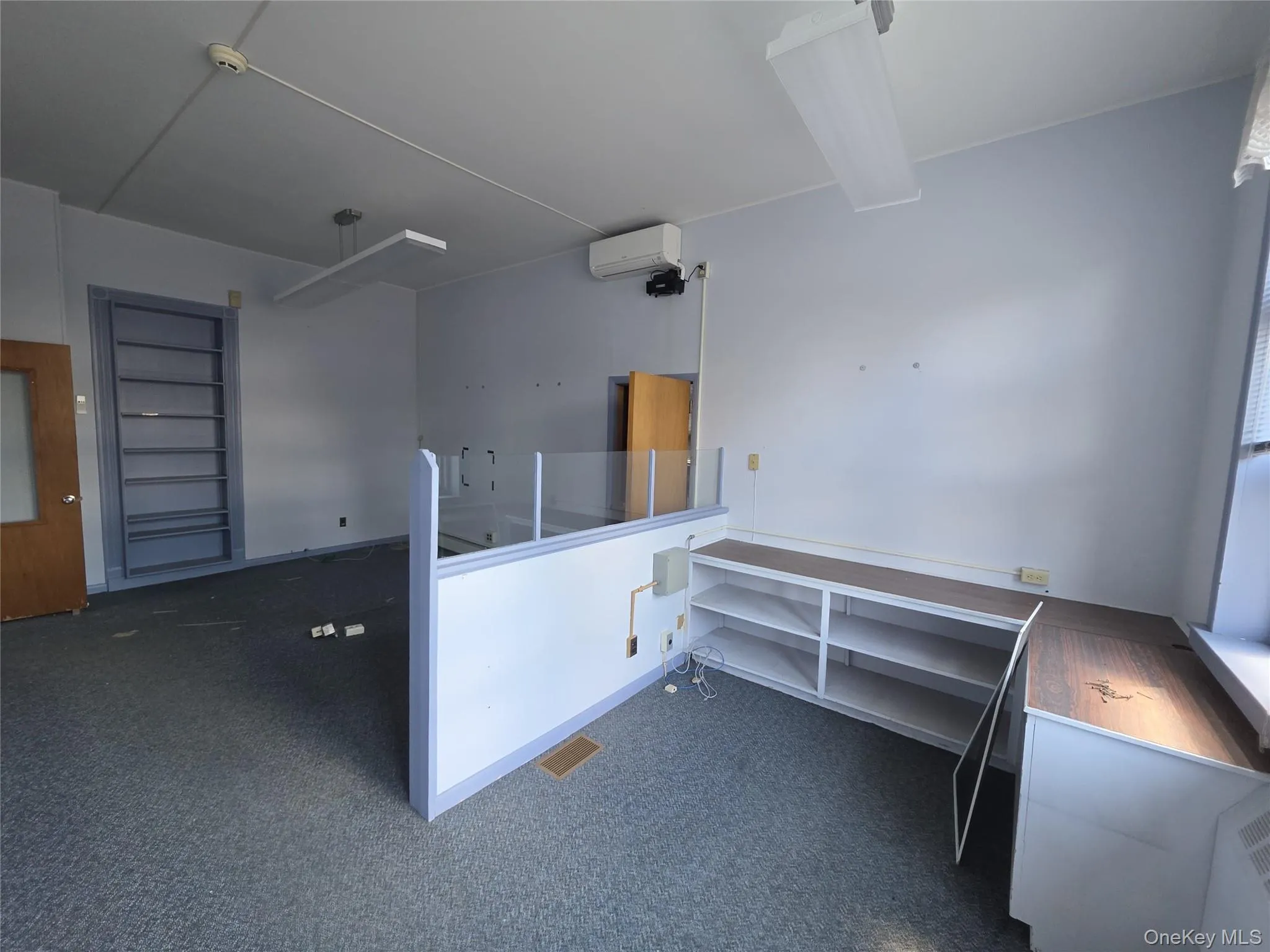 Interior room featuring built-in shelving, carpet flooring, and a partition wall with clear paneling Interior room featuring built-in shelving, carpet flooring, and a partition wall with clear paneling