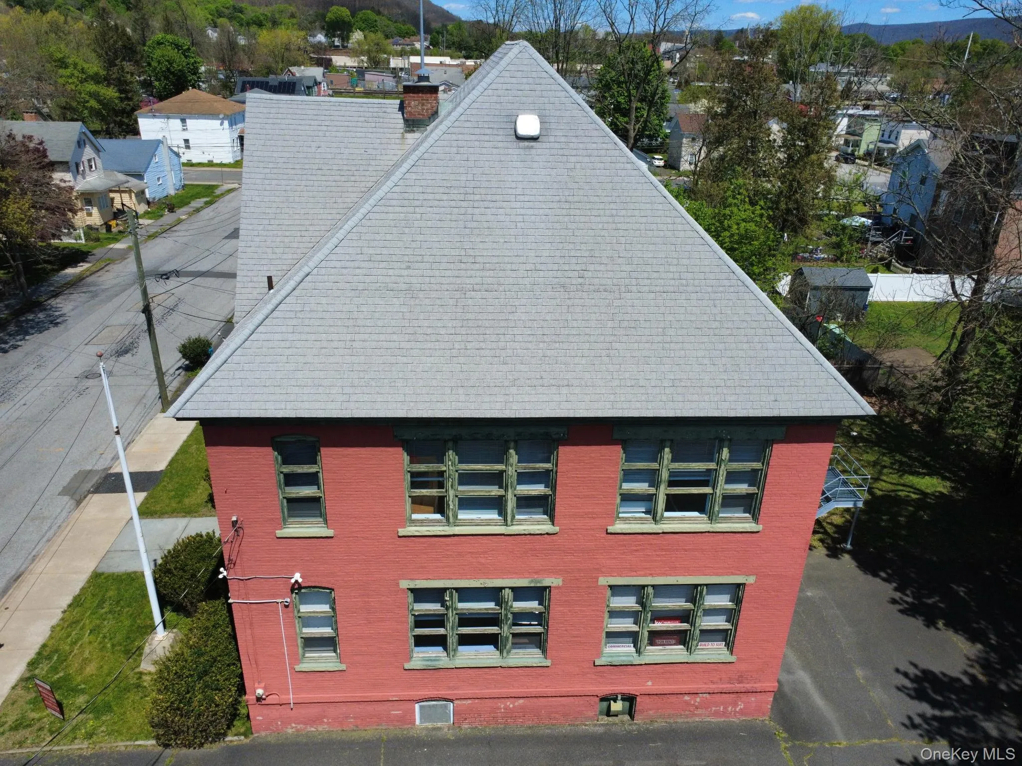 Brick exterior featuring a gray shingle roof and multiple windows with green trim Brick exterior featuring a gray shingle roof and multiple windows with green trim