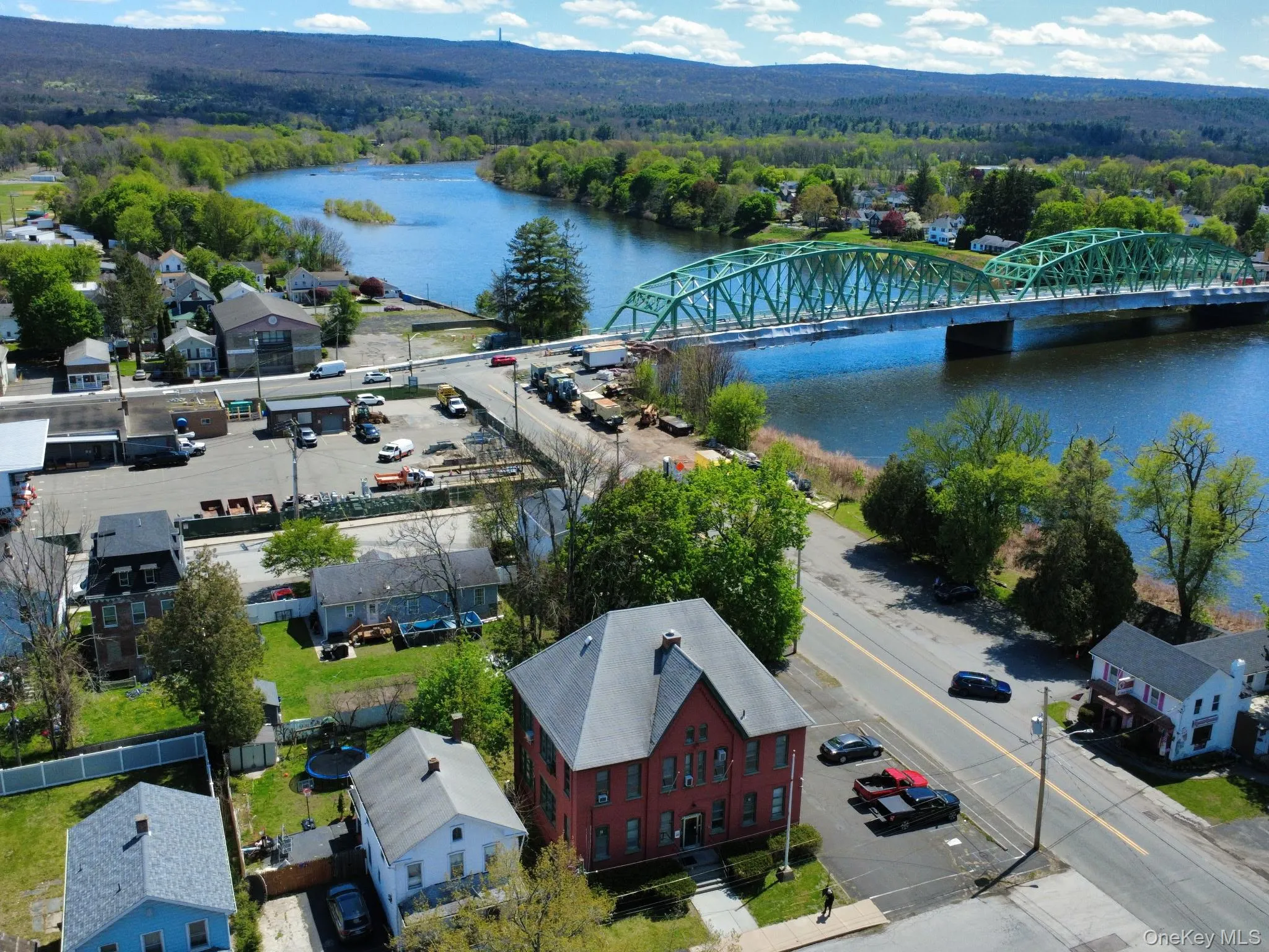Waterfront setting featuring a prominent green truss bridge, a broad river, and distant wooded hills Waterfront setting featuring a prominent green truss bridge, a broad river, and distant wooded hills