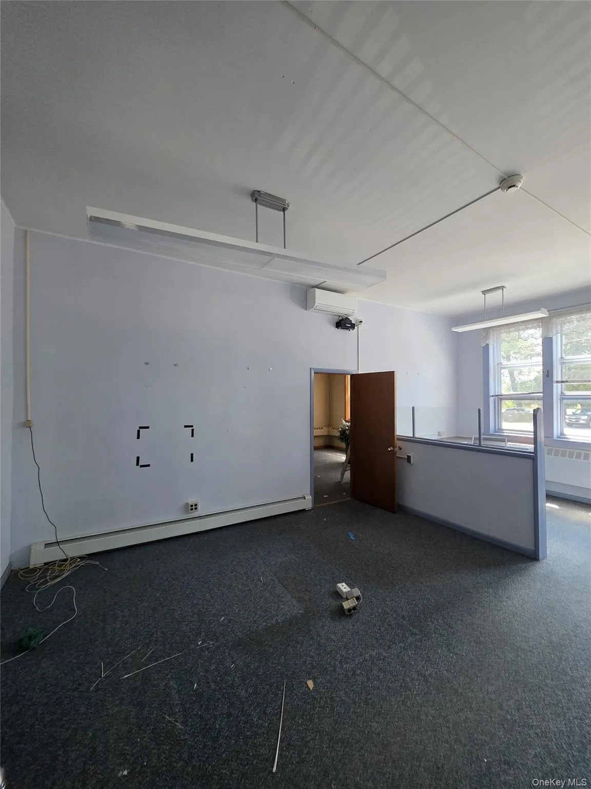 Open-plan room featuring wall-to-wall carpeting, multiple linear fluorescent light fixtures, and a half-wall partition Open-plan room featuring wall-to-wall carpeting, multiple linear fluorescent light fixtures, and a half-wall partition