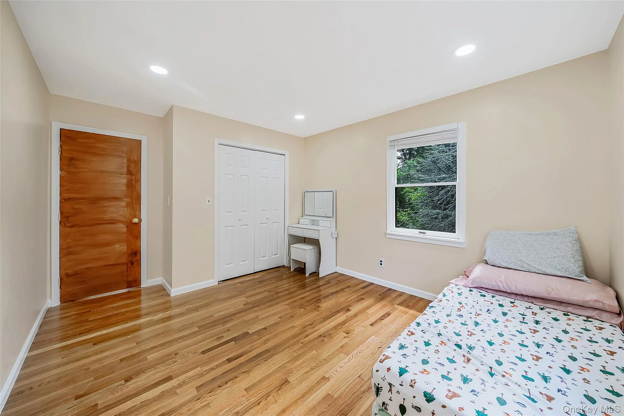 Room featuring wood-finish flooring, recessed lighting, a window, a bi-fold closet, and a wood panel door Room featuring wood-finish flooring, recessed lighting, a window, a bi-fold closet, and a wood panel door