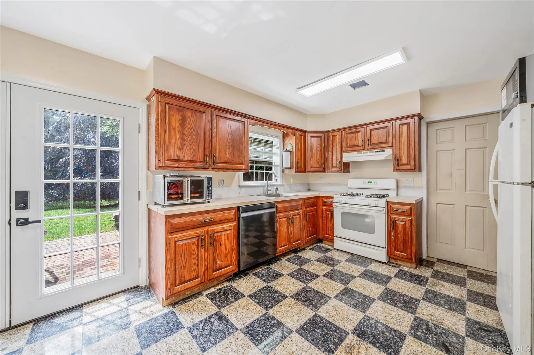 Kitchen featuring wood cabinetry, checkerboard-patterned flooring, white appliances, and a glass-paneled exterior door Kitchen featuring wood cabinetry, checkerboard-patterned flooring, white appliances, and a glass-paneled exterior door