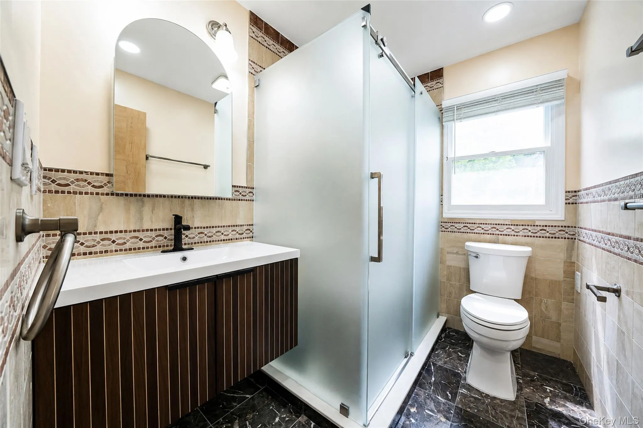 Floating vanity with a white countertop and matte black fixtures, an arched mirror, and a frosted glass shower enclosure Floating vanity with a white countertop and matte black fixtures, an arched mirror, and a frosted glass shower enclosure
