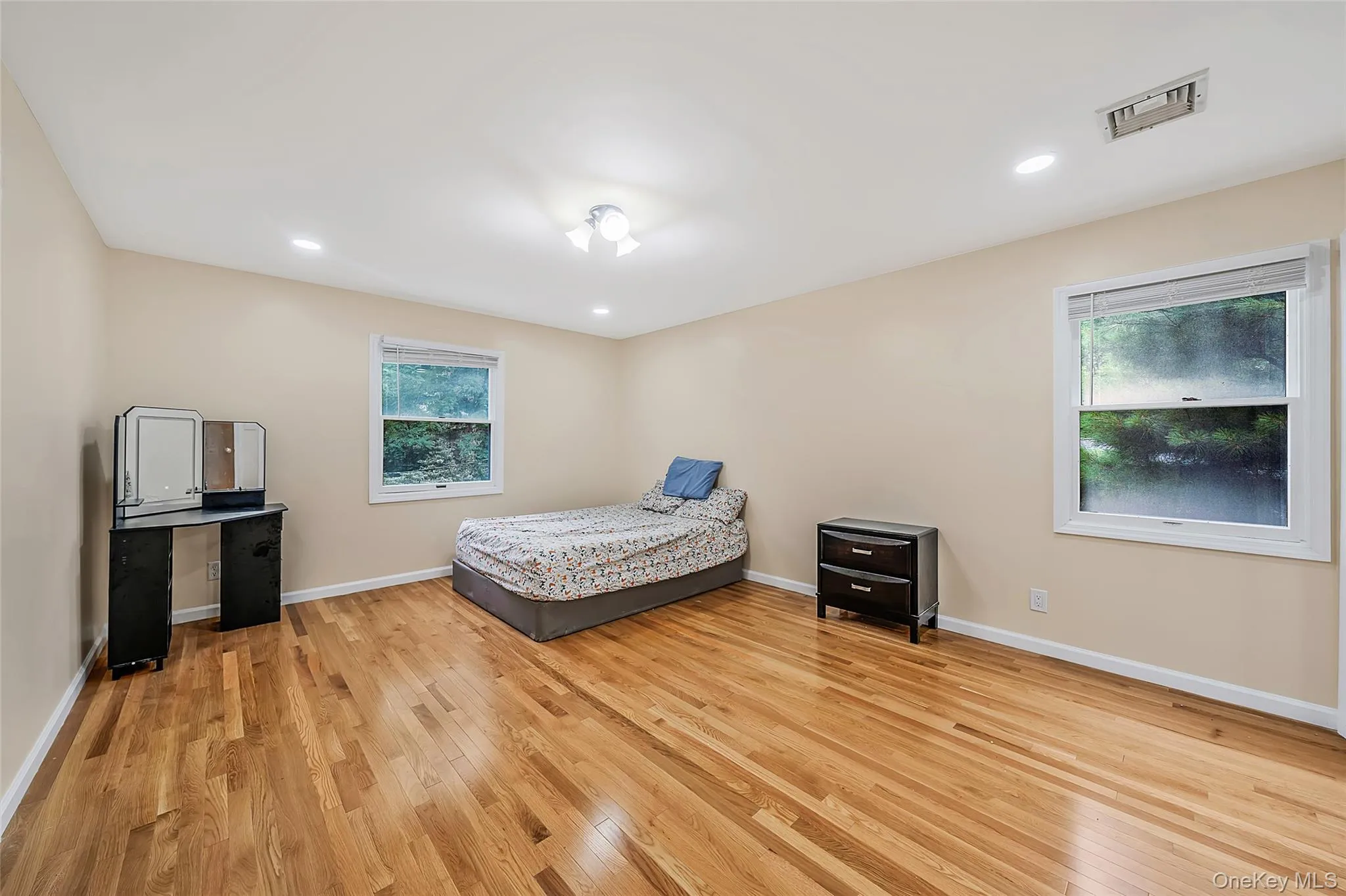 Spacious interior room featuring wood-finish flooring, recessed lighting, neutral wall tones, and two large windows Spacious interior room featuring wood-finish flooring, recessed lighting, neutral wall tones, and two large windows