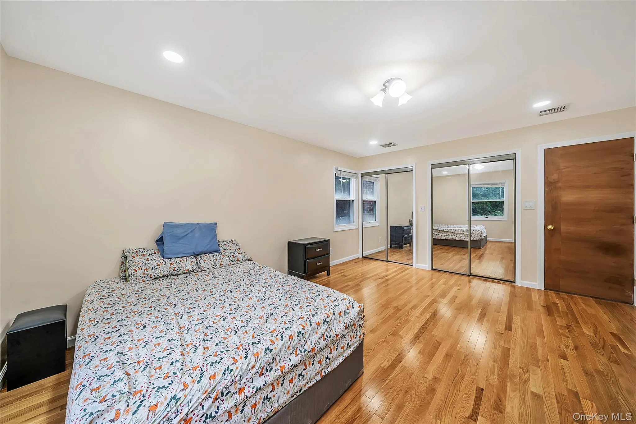 Bedroom featuring wood-finish flooring, two sets of mirrored sliding closet doors, and recessed lighting Bedroom featuring wood-finish flooring, two sets of mirrored sliding closet doors, and recessed lighting
