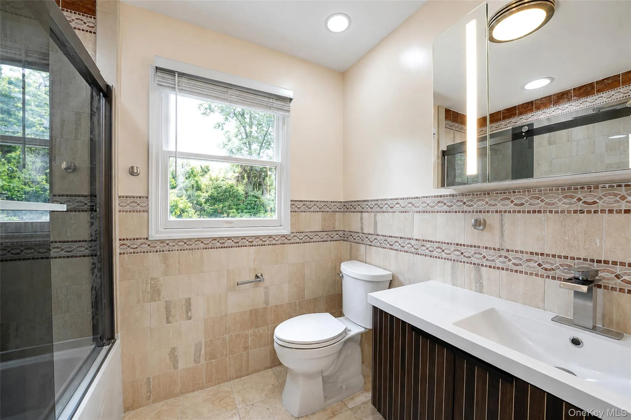 Contemporary bathroom featuring a dark wood-finish vanity with an integrated white sink, a wall-mounted mirrored medicine cabinet with integrated lighting, and a walk-in shower with a glass enclosure Contemporary bathroom featuring a dark wood-finish vanity with an integrated white sink, a wall-mounted mirrored medicine cabinet with integrated lighting, and a walk-in shower with a glass enclosure