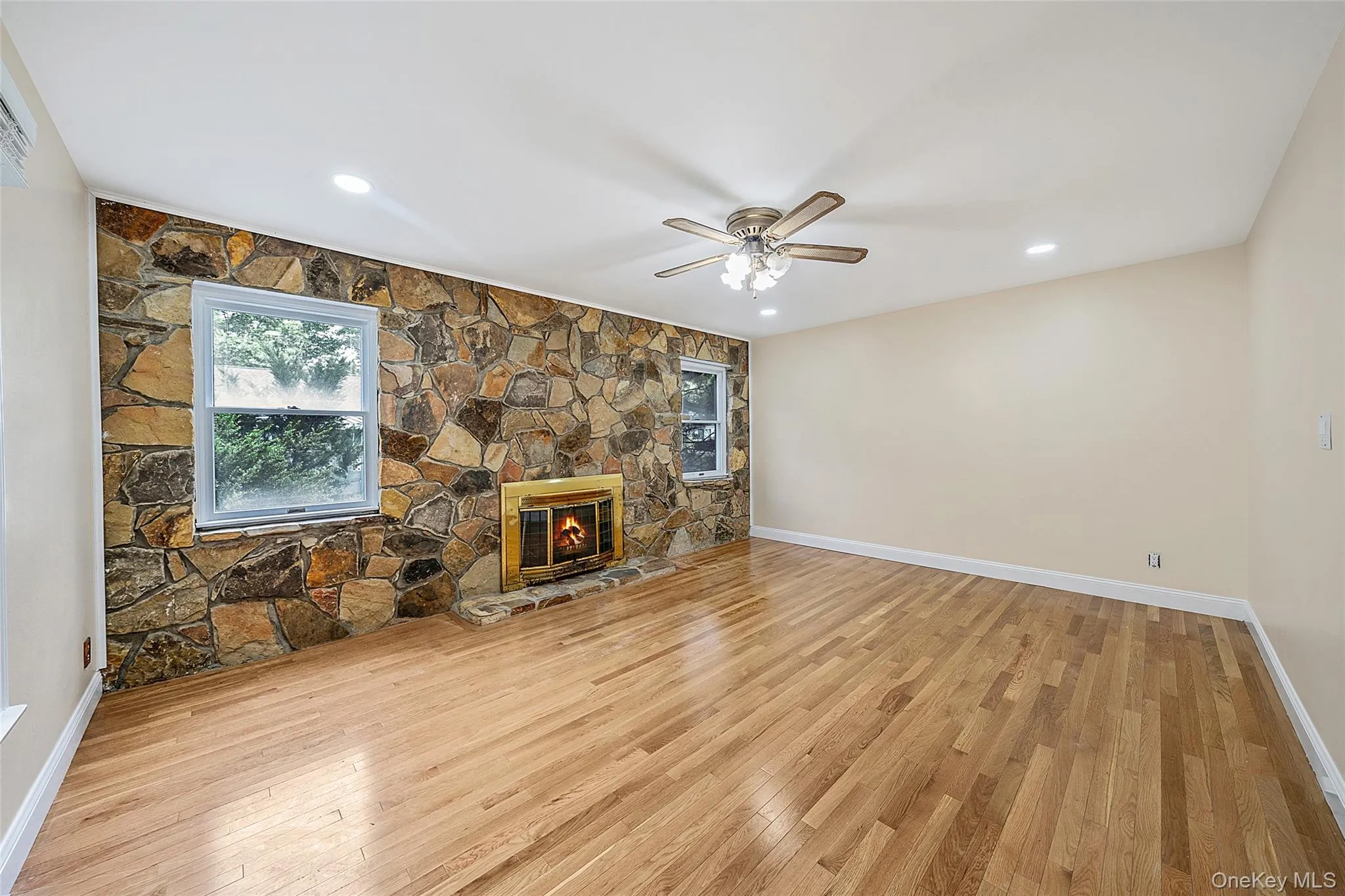 Spacious room featuring a prominent stone accent wall with an integrated fireplace and two windows Spacious room featuring a prominent stone accent wall with an integrated fireplace and two windows
