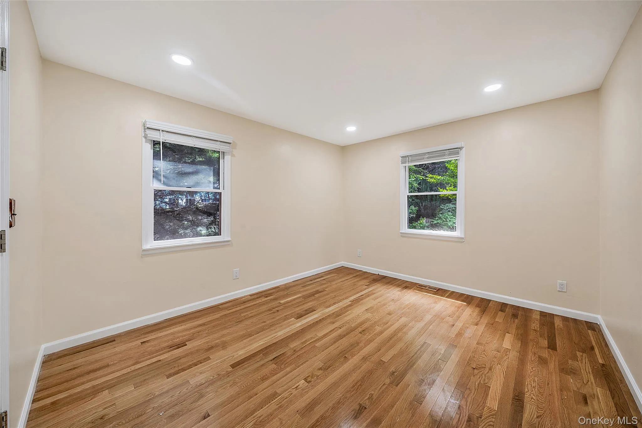 Hardwood flooring throughout featuring two windows with white blinds, recessed lighting, and a neutral wall color Hardwood flooring throughout featuring two windows with white blinds, recessed lighting, and a neutral wall color