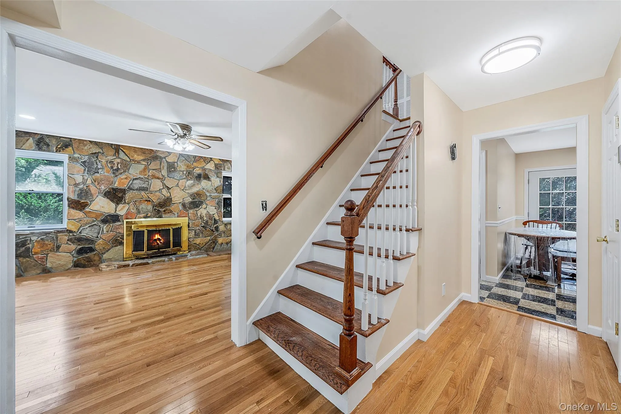 Entryway featuring wood-finish flooring, a staircase with wood treads and white risers, and a stone-clad fireplace wall visible through an open doorway Entryway featuring wood-finish flooring, a staircase with wood treads and white risers, and a stone-clad fireplace wall visible through an open doorway