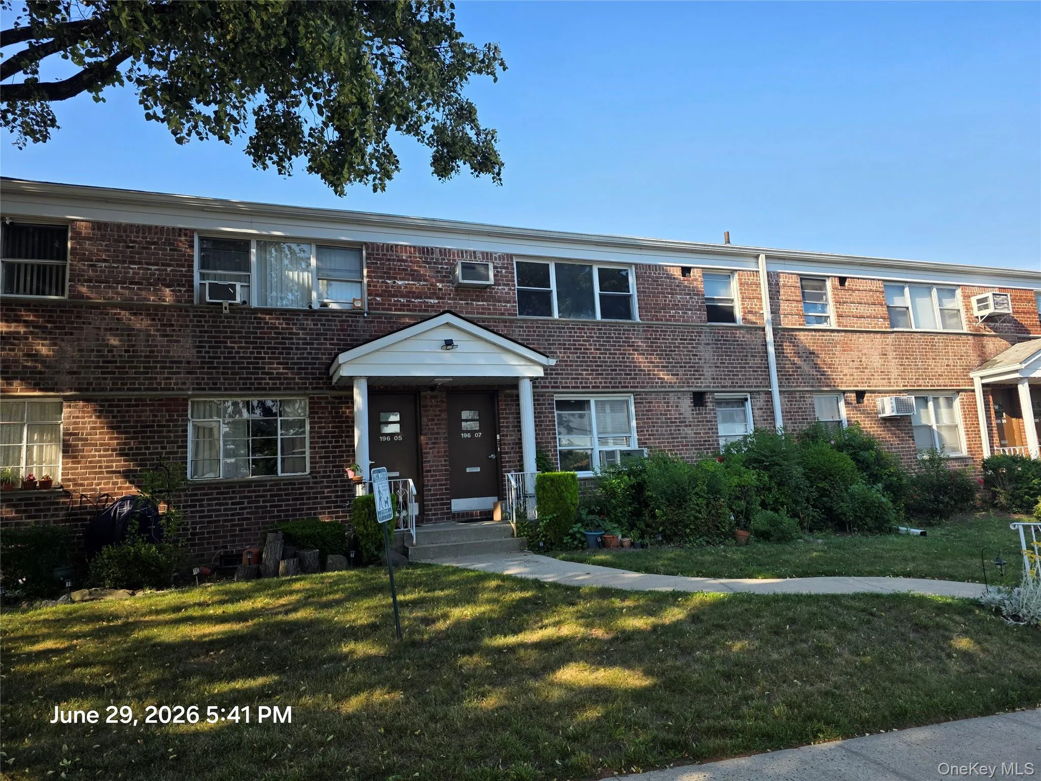 Two-story brick facade building featuring multiple windows, a covered entry with white columns, and a grassy front yard with established plantings Two-story brick facade building featuring multiple windows, a covered entry with white columns, and a grassy front yard with established plantings