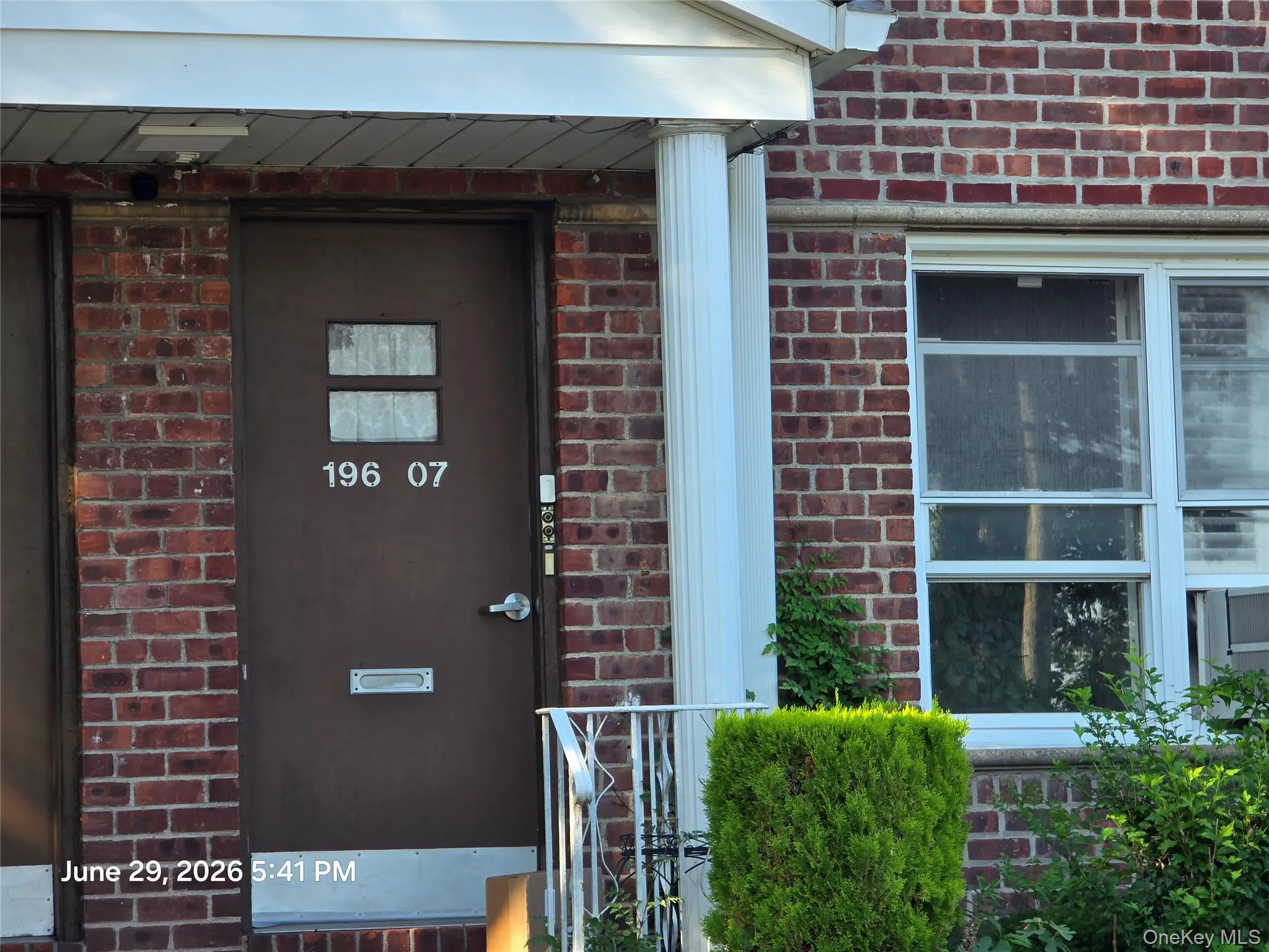 Brick exterior featuring a brown entry door with transom windows, a white pillar, and a white window frame Brick exterior featuring a brown entry door with transom windows, a white pillar, and a white window frame