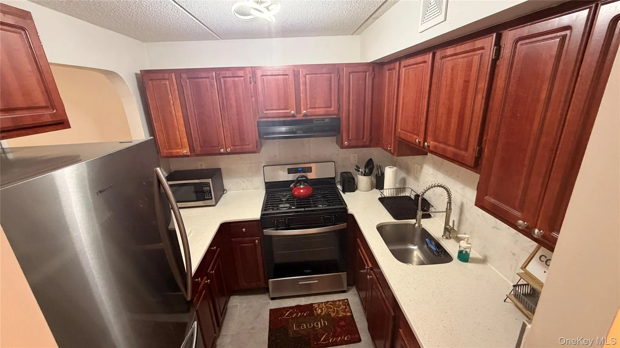 U-shaped kitchen featuring wood cabinetry, light-toned countertops, and a full suite of stainless steel appliances U-shaped kitchen featuring wood cabinetry, light-toned countertops, and a full suite of stainless steel appliances