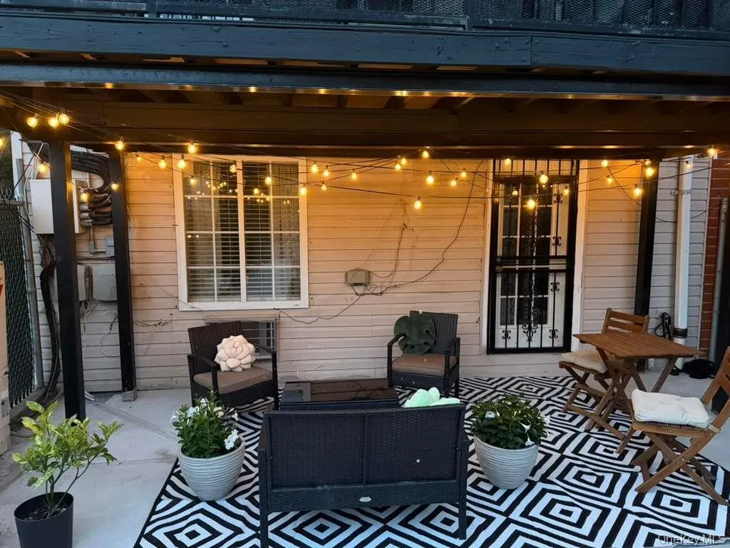 Covered patio featuring a black and white geometric outdoor rug, horizontal siding, a window with horizontal blinds, and a door with security grating Covered patio featuring a black and white geometric outdoor rug, horizontal siding, a window with horizontal blinds, and a door with security grating