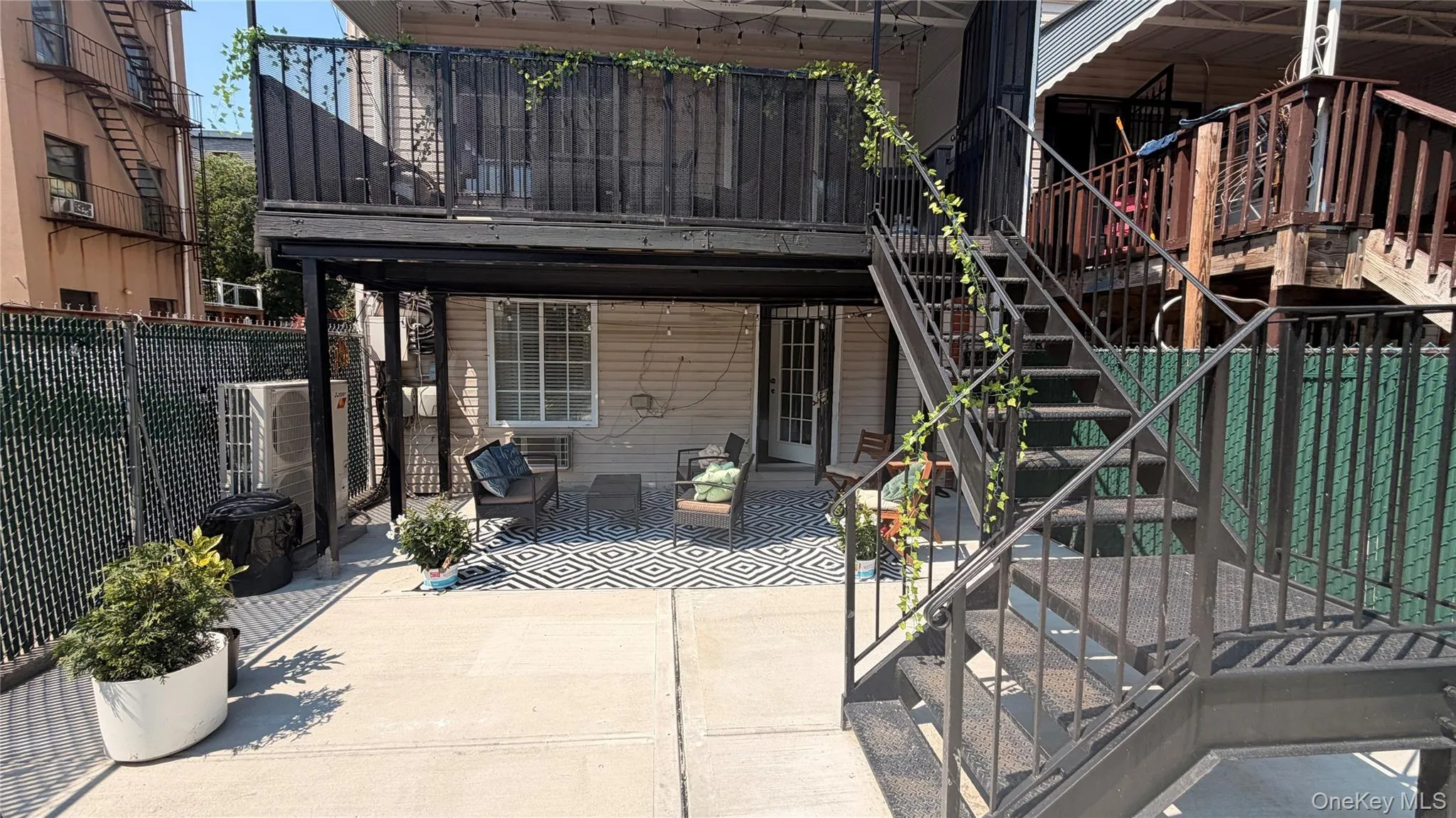 Multi-level outdoor patio featuring a concrete slab, chain-link fencing, and black metal staircase with railings Multi-level outdoor patio featuring a concrete slab, chain-link fencing, and black metal staircase with railings
