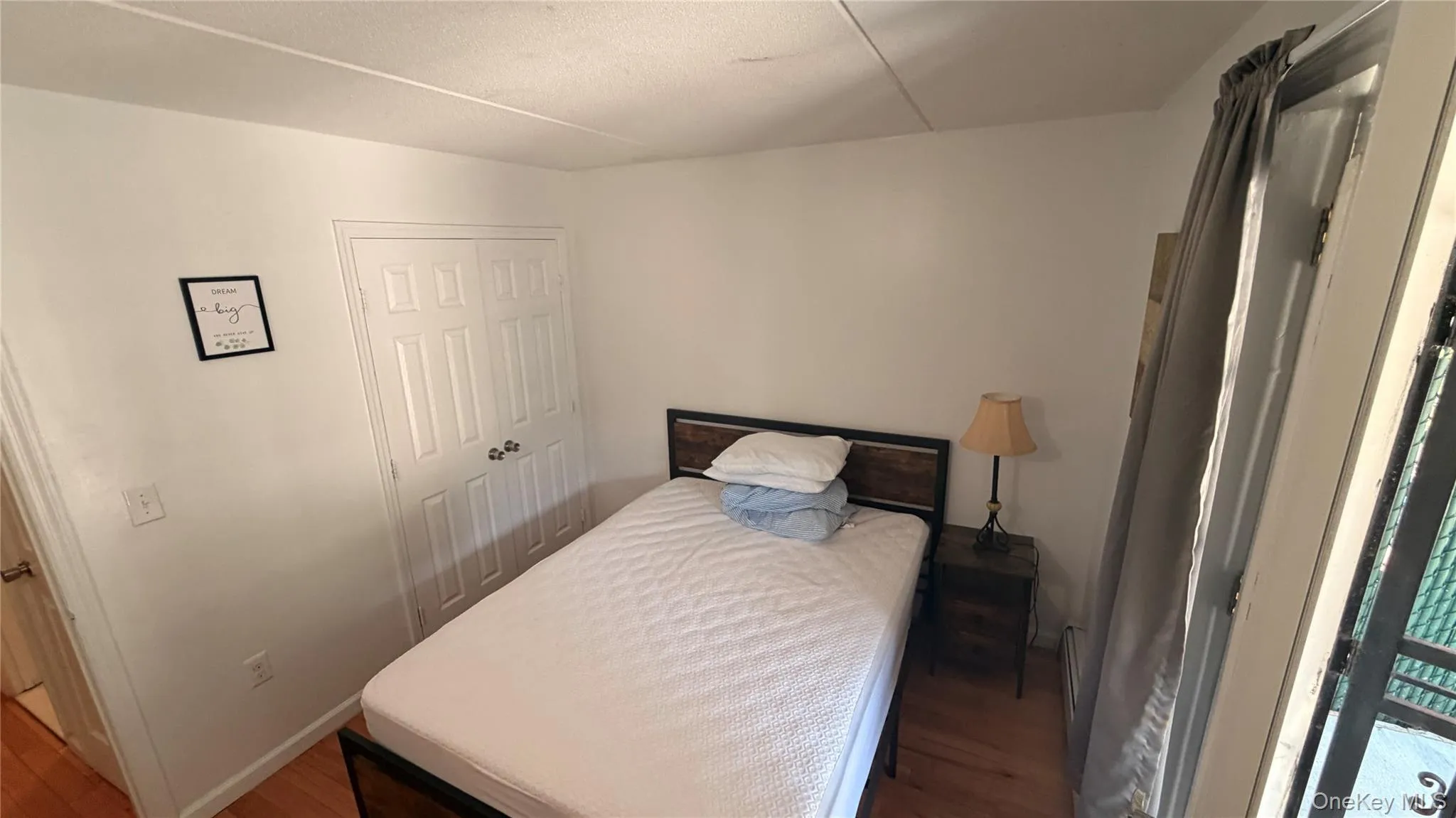 Bright interior space featuring a double-door closet with louvered panels, light-colored walls, and wood-finish flooring Bright interior space featuring a double-door closet with louvered panels, light-colored walls, and wood-finish flooring