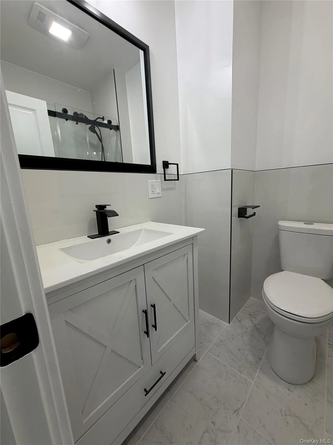 half Bathroom featuring a white vanity with cross-brace detailing, matte black hardware, and a white integrated sink with a black waterfall faucet half Bathroom featuring a white vanity with cross-brace detailing, matte black hardware, and a white integrated sink with a black waterfall faucet
