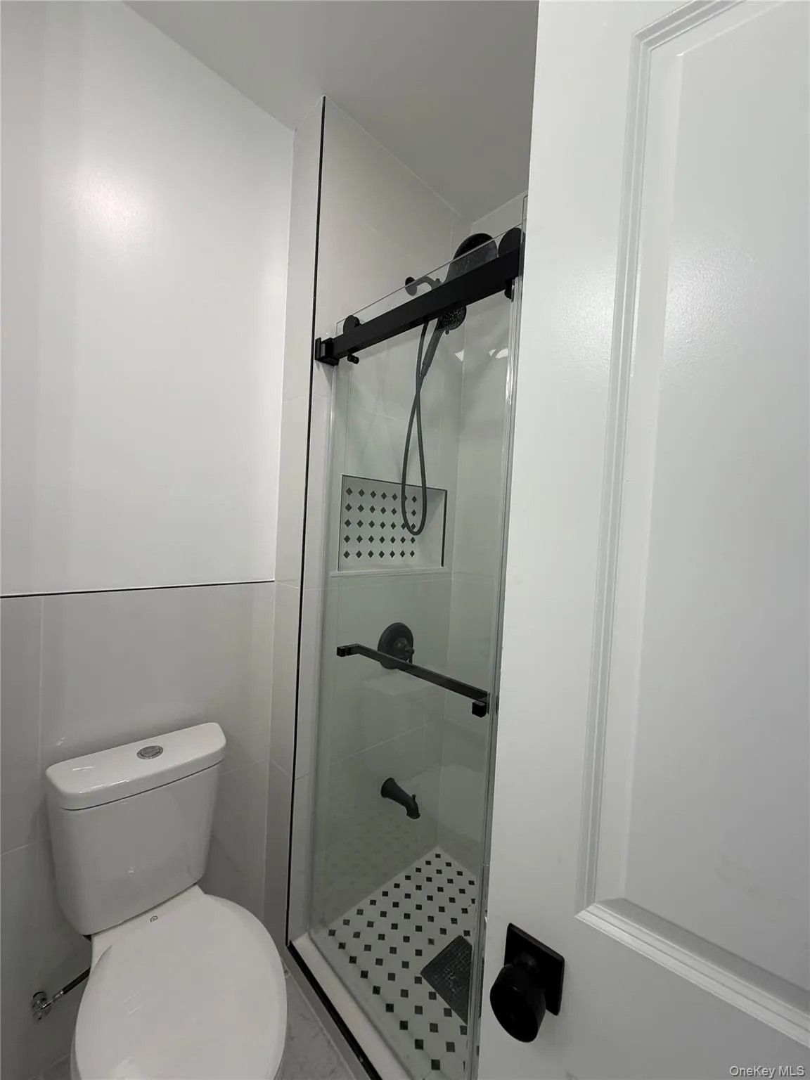 Shower enclosure with clear glass panel, matte black hardware, and an integrated tiled niche Shower enclosure with clear glass panel, matte black hardware, and an integrated tiled niche