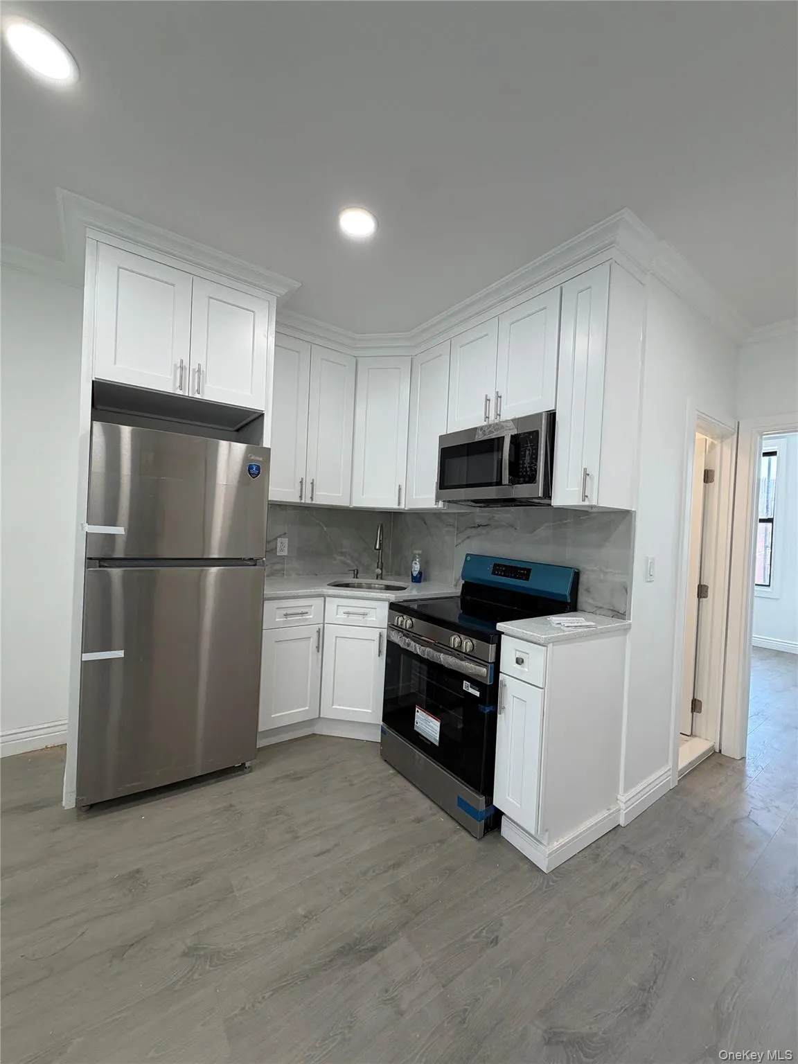 Modern kitchen featuring white shaker cabinetry, stainless steel appliances, and wood-finish flooring Modern kitchen featuring white shaker cabinetry, stainless steel appliances, and wood-finish flooring