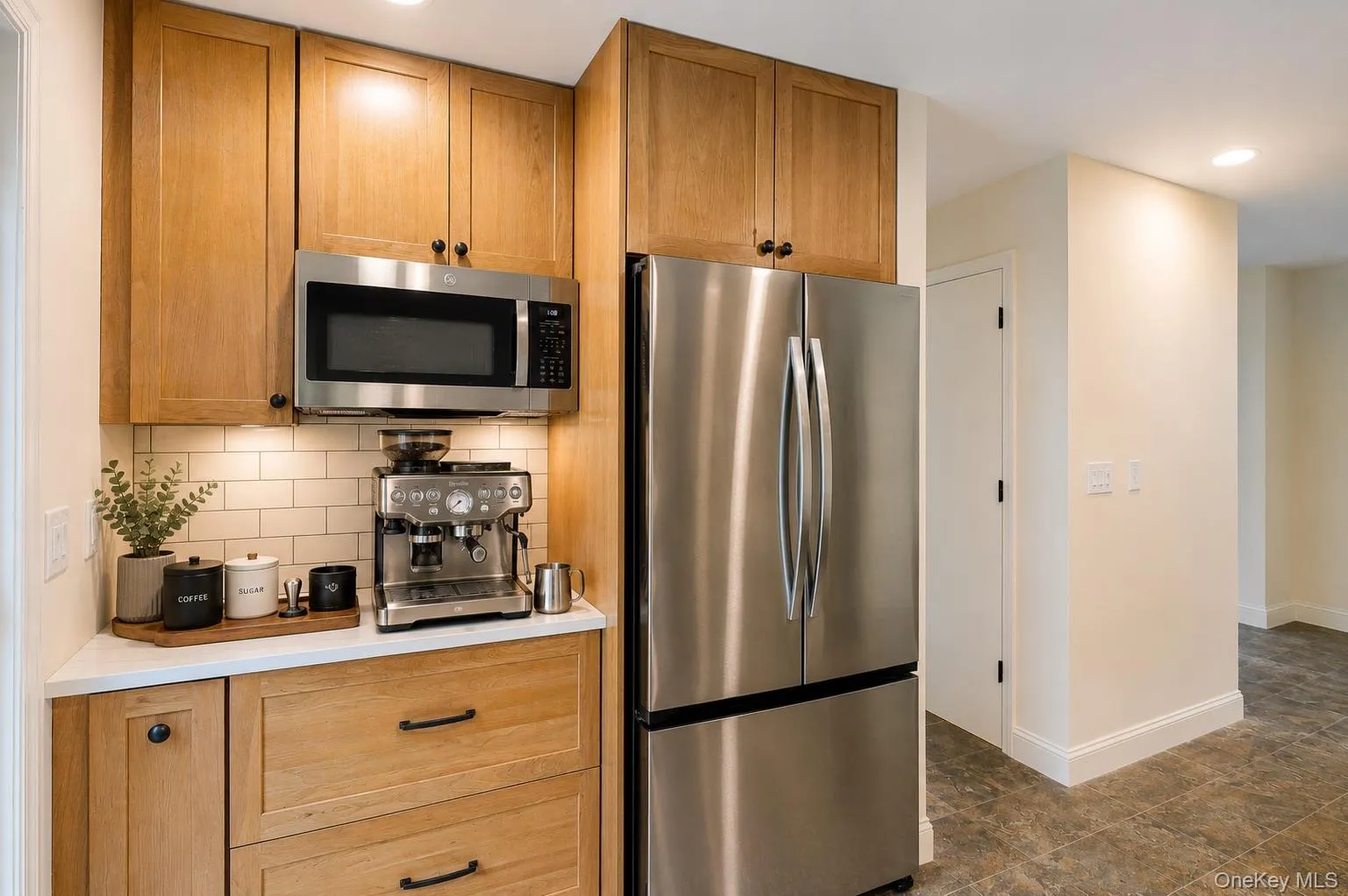 Stainless steel French door refrigerator, wood cabinetry with black hardware, subway tile backsplash, under-cabinet lighting, and stone-finish flooring. This image has been digitally enhanced for visualization purposes to demonstrate potential furnishings, décor, and space planning. Actual property is conveyed unfurnished unless otherwise noted. Stainless steel French door refrigerator, wood cabinetry with black hardware, subway tile backsplash, under-cabinet lighting, and stone-finish flooring. This image has been digitally enhanced for visualization purposes to demonstrate potential furnishings, décor, and space planning. Actual property is conveyed unfurnished unless otherwise noted.