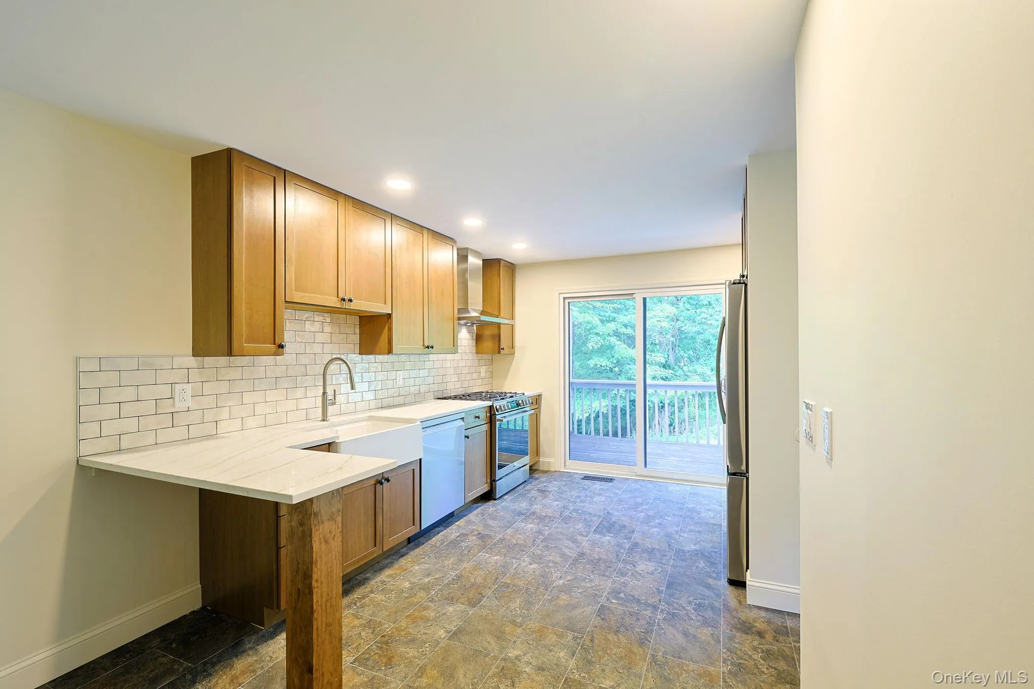 Kitchen featuring wood cabinetry, white subway tile backsplash, stainless steel appliances, and a farmhouse sink Kitchen featuring wood cabinetry, white subway tile backsplash, stainless steel appliances, and a farmhouse sink
