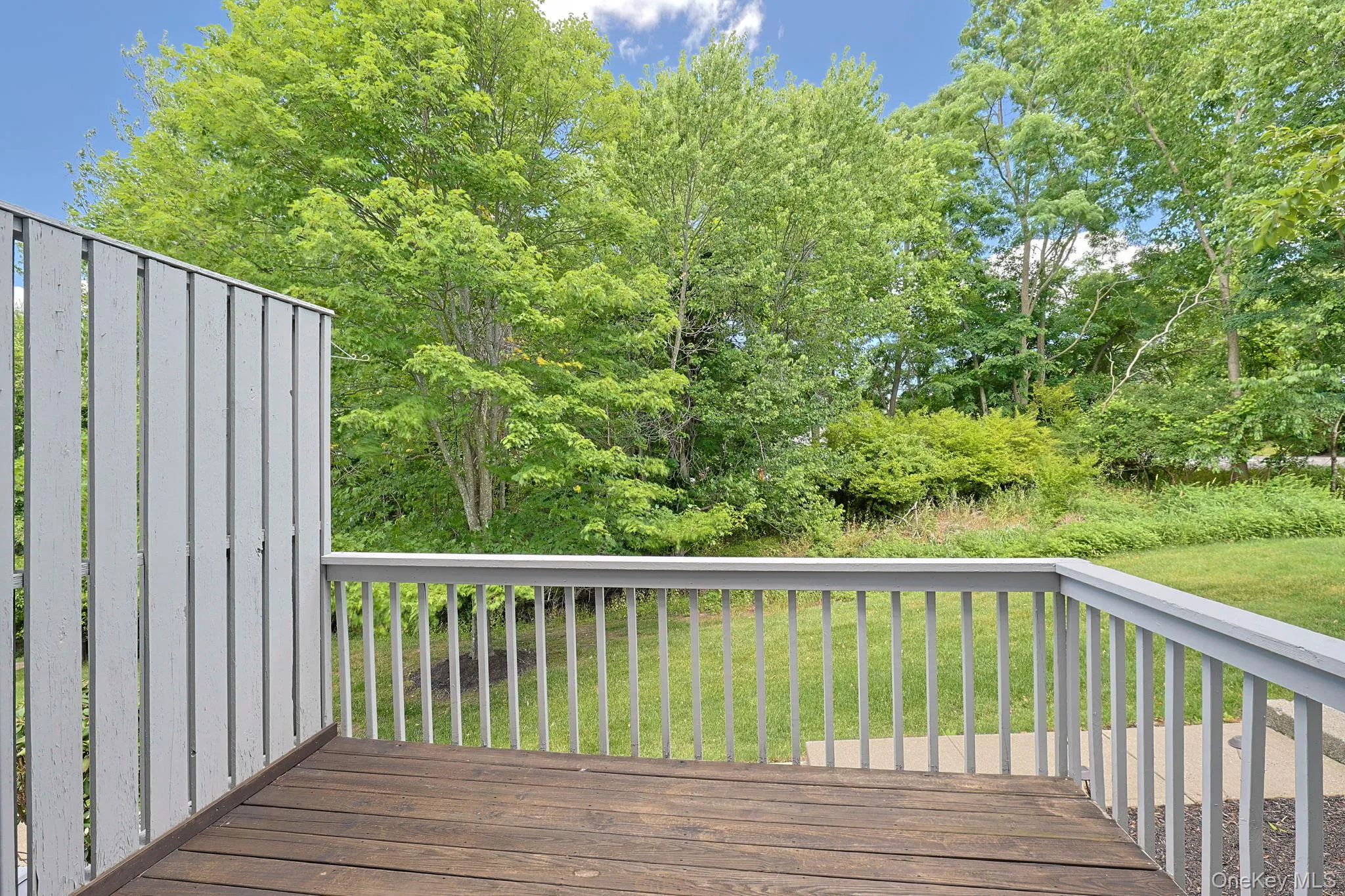 Outdoor deck featuring wood-finish flooring, light gray railings, and a privacy wall Outdoor deck featuring wood-finish flooring, light gray railings, and a privacy wall