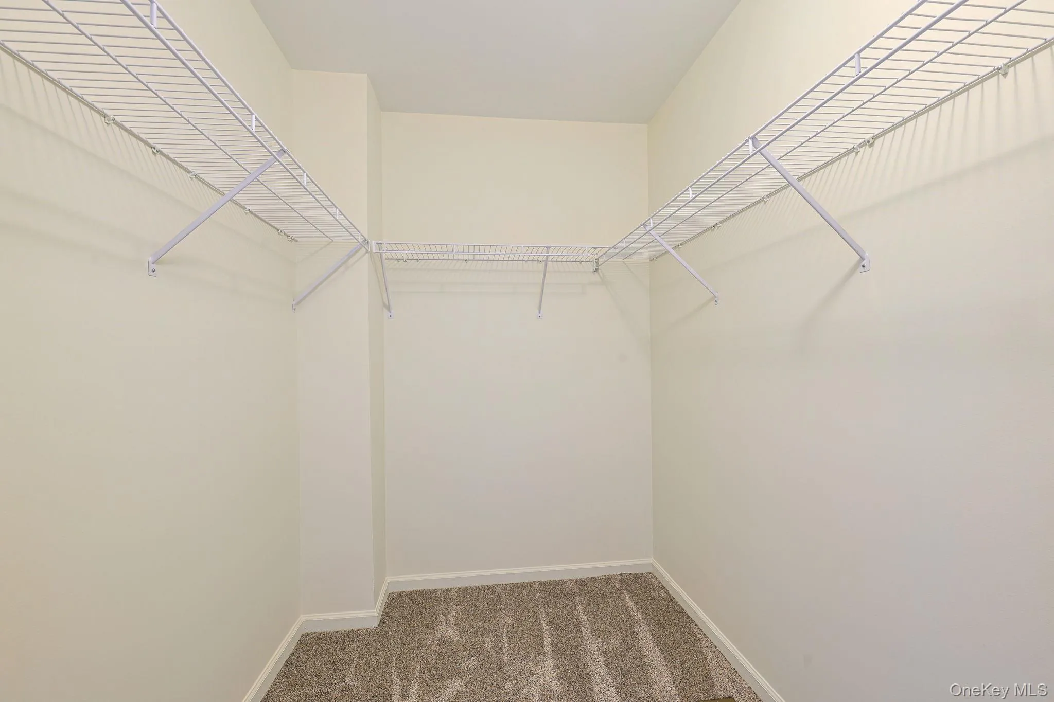 Walk-in closet with wire shelving system, light-colored walls, and neutral carpet flooring Walk-in closet with wire shelving system, light-colored walls, and neutral carpet flooring
