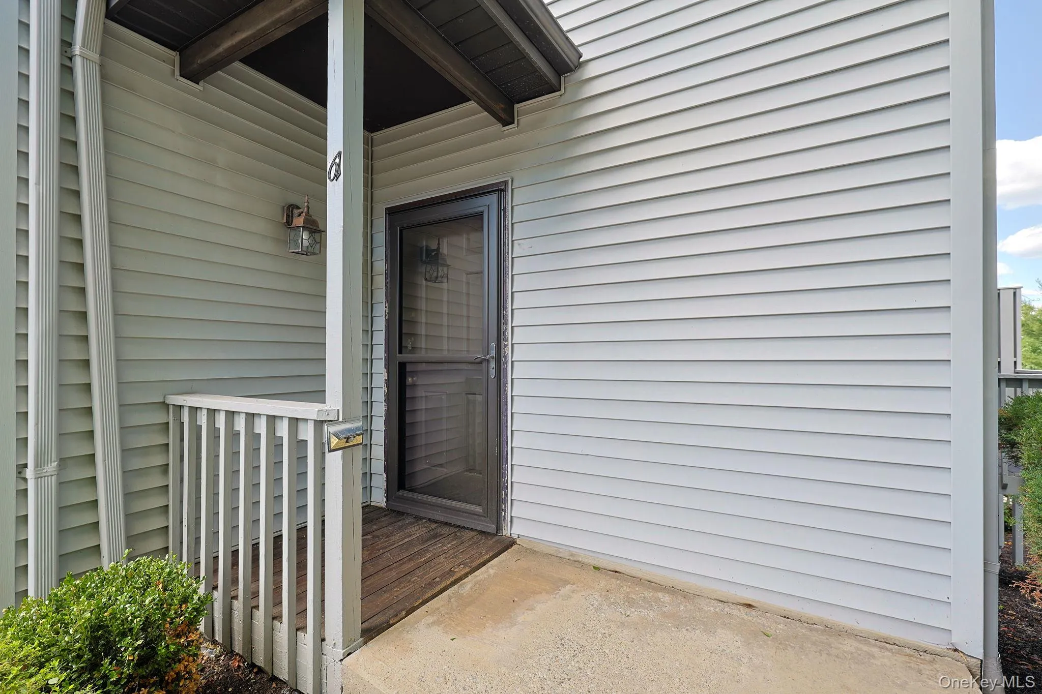 Entryway featuring light-colored horizontal siding, a covered porch with wood-finish flooring, a white railing, and an exterior lantern fixture Entryway featuring light-colored horizontal siding, a covered porch with wood-finish flooring, a white railing, and an exterior lantern fixture