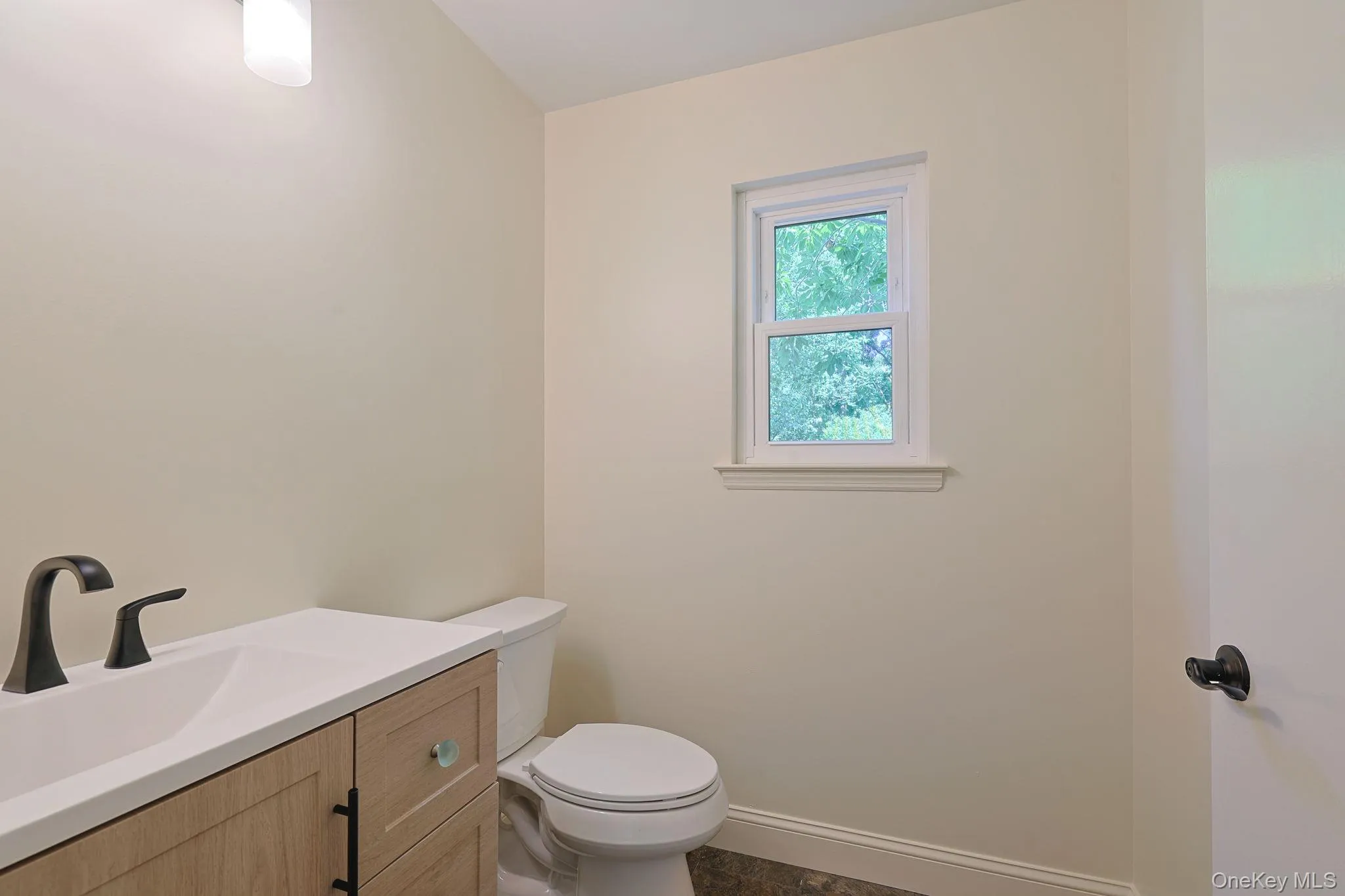 Powder room featuring a wood-finish vanity with an integrated sink, matte black faucet, and a window for natural light Powder room featuring a wood-finish vanity with an integrated sink, matte black faucet, and a window for natural light