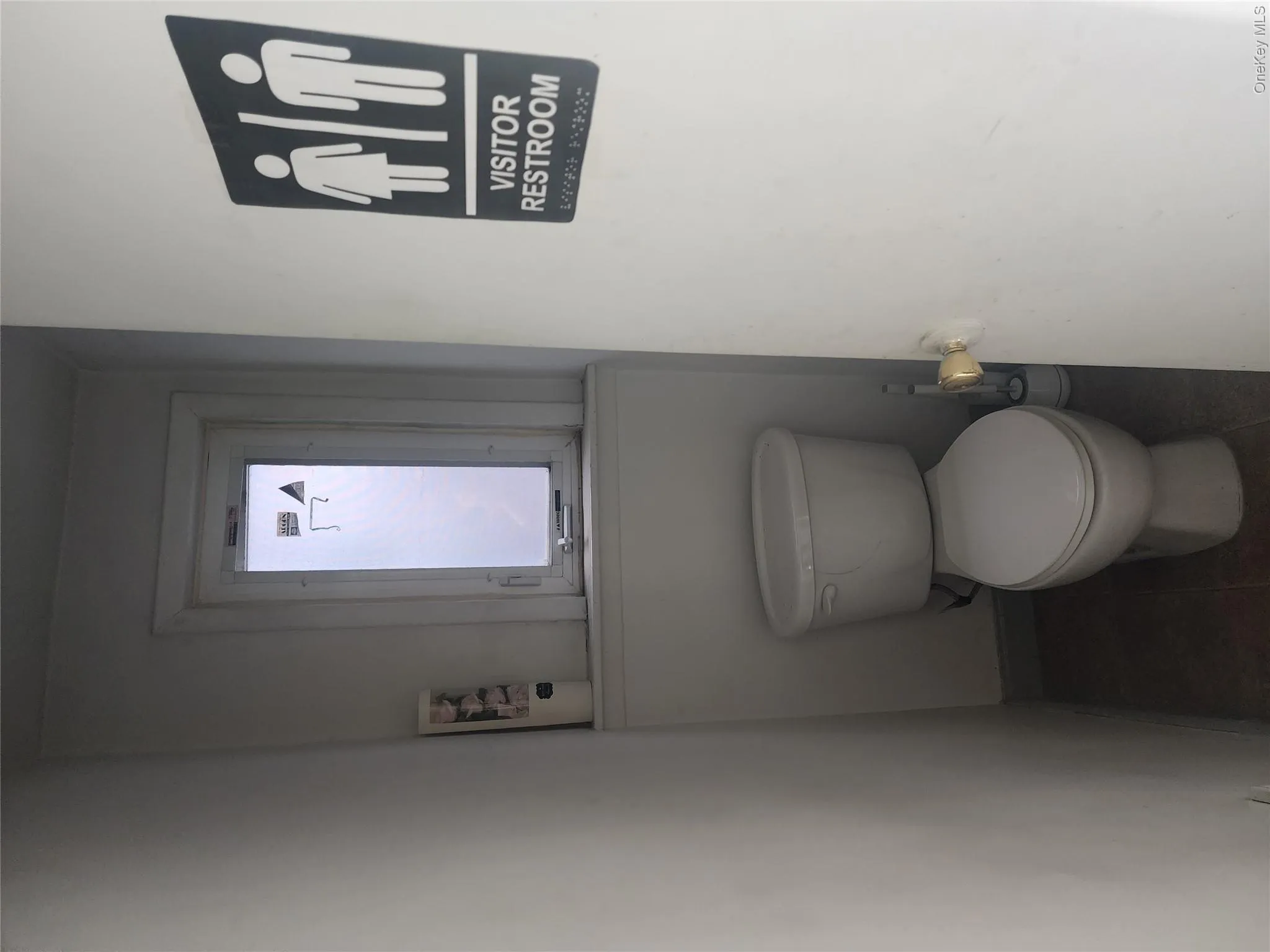 Compact restroom featuring a white toilet, frosted privacy window, and dark flooring Compact restroom featuring a white toilet, frosted privacy window, and dark flooring