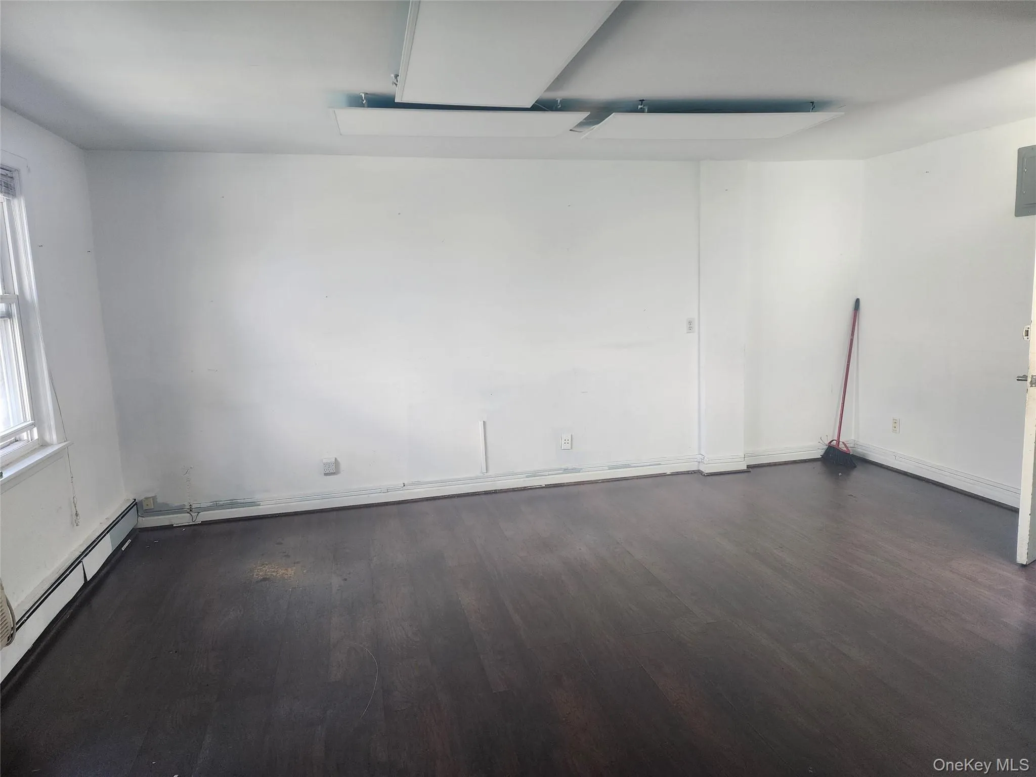 Interior room featuring dark wood-finish flooring, white painted walls, and a window with white trim Interior room featuring dark wood-finish flooring, white painted walls, and a window with white trim