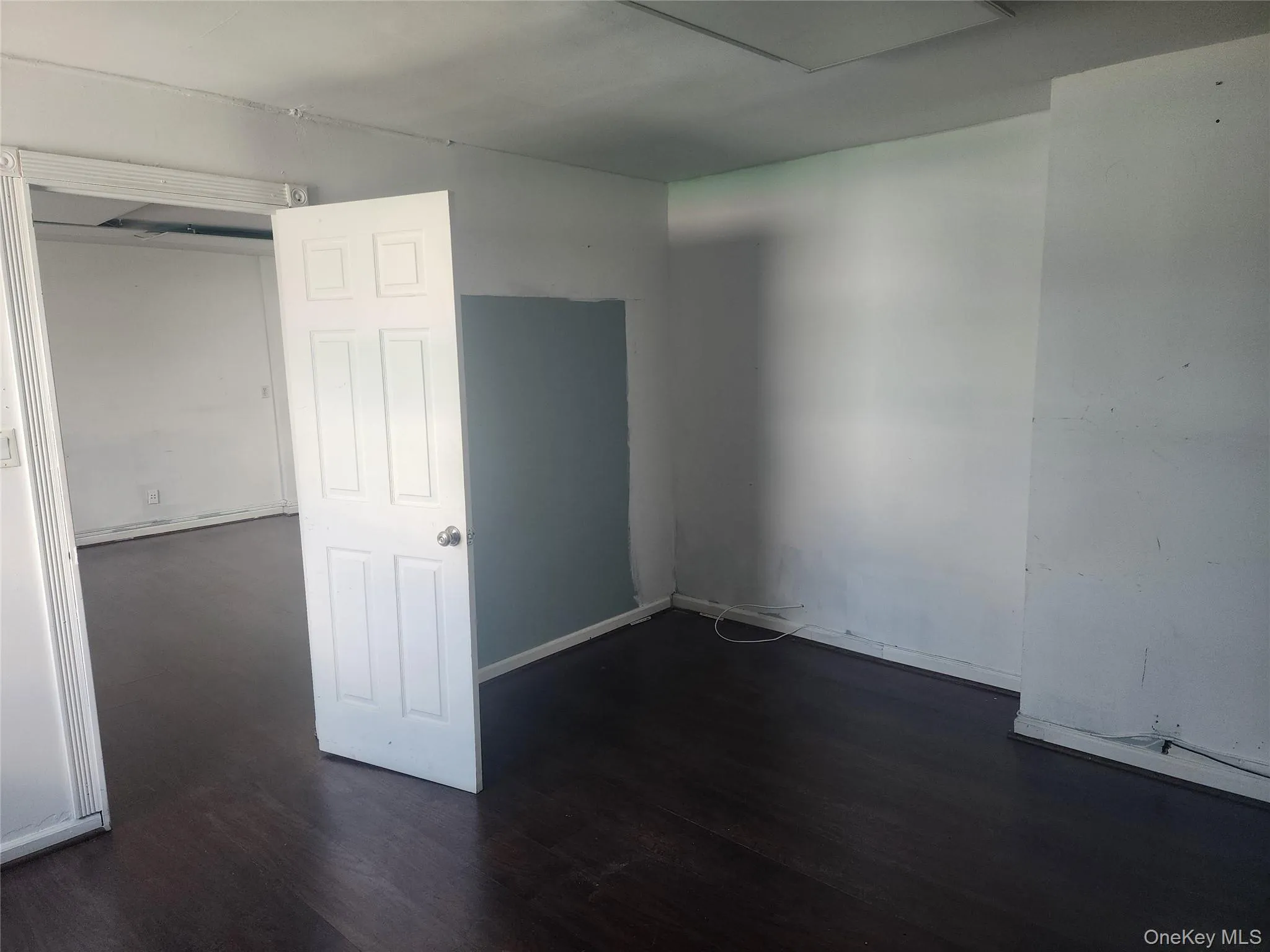 Interior space featuring dark wood-finish flooring, white walls, and a partial accent wall with a blue-gray finish Interior space featuring dark wood-finish flooring, white walls, and a partial accent wall with a blue-gray finish