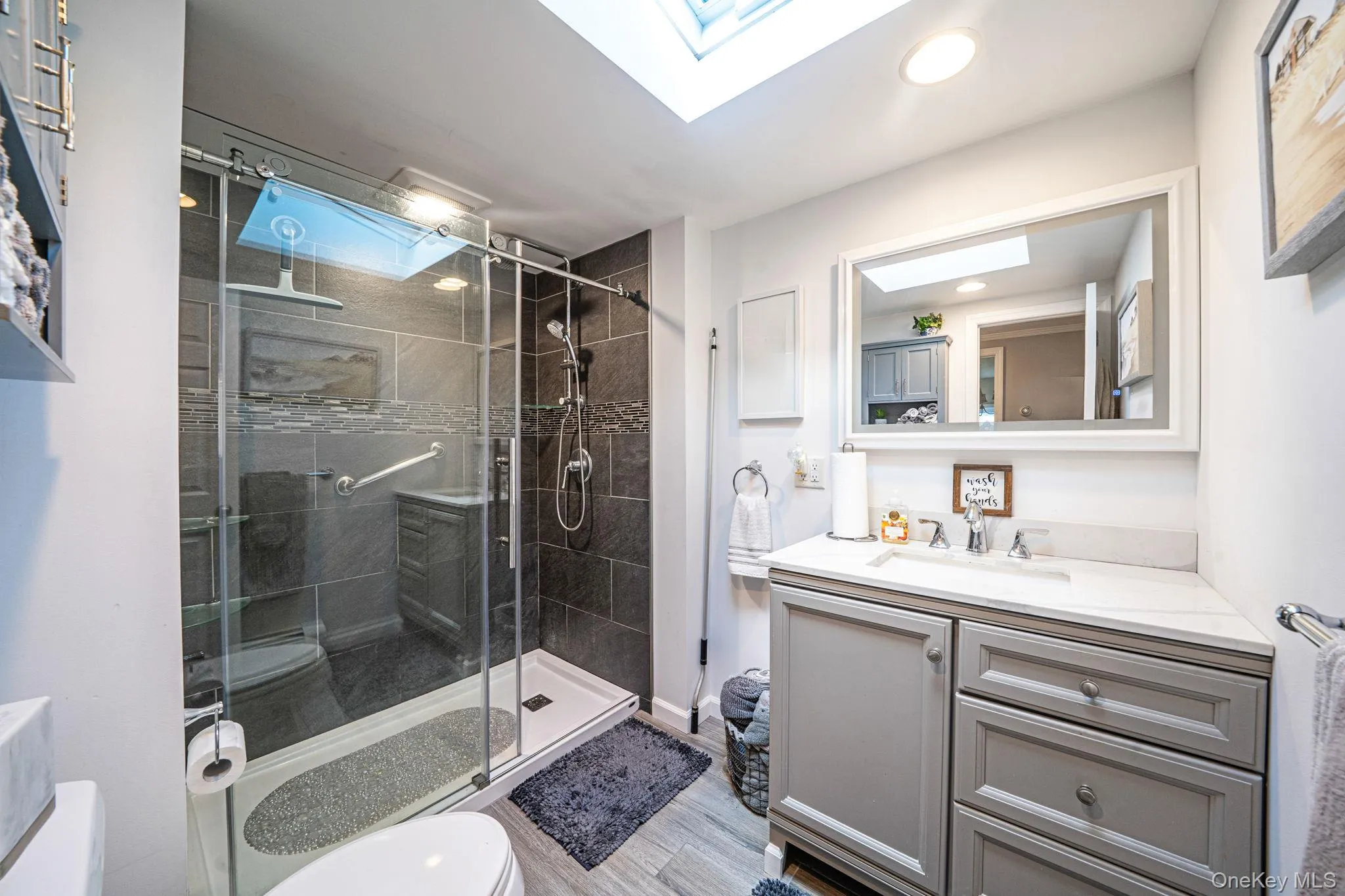 Contemporary bathroom featuring a glass-enclosed shower with dark tile surround, a built-in grab bar, and a rain shower head Contemporary bathroom featuring a glass-enclosed shower with dark tile surround, a built-in grab bar, and a rain shower head