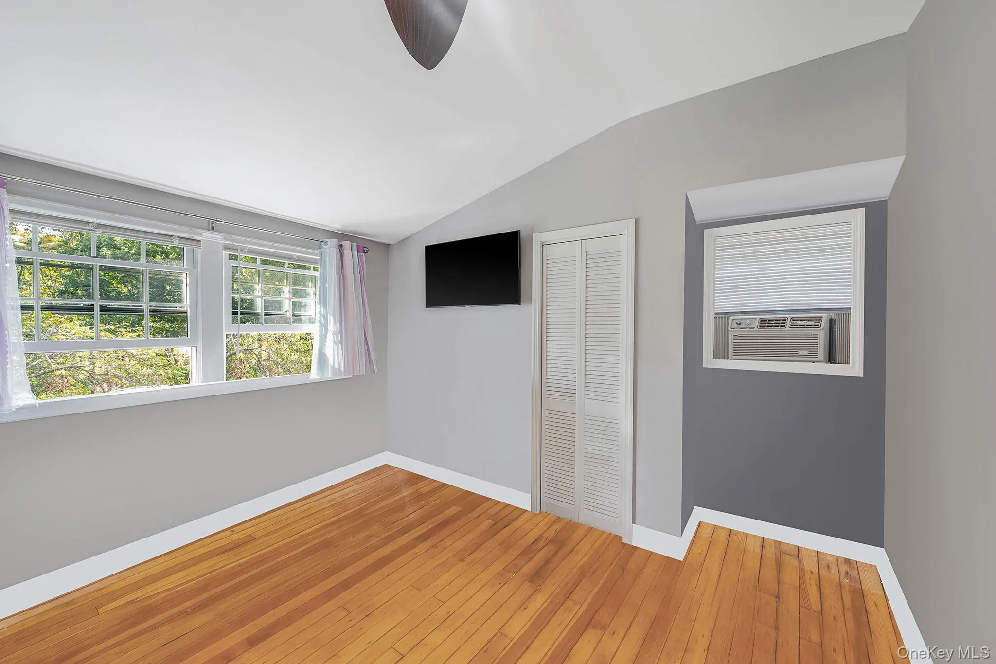 Bedroom featuring wood-finish flooring, multiple windows, a ceiling fan, and a built-in air conditioning unit Bedroom featuring wood-finish flooring, multiple windows, a ceiling fan, and a built-in air conditioning unit