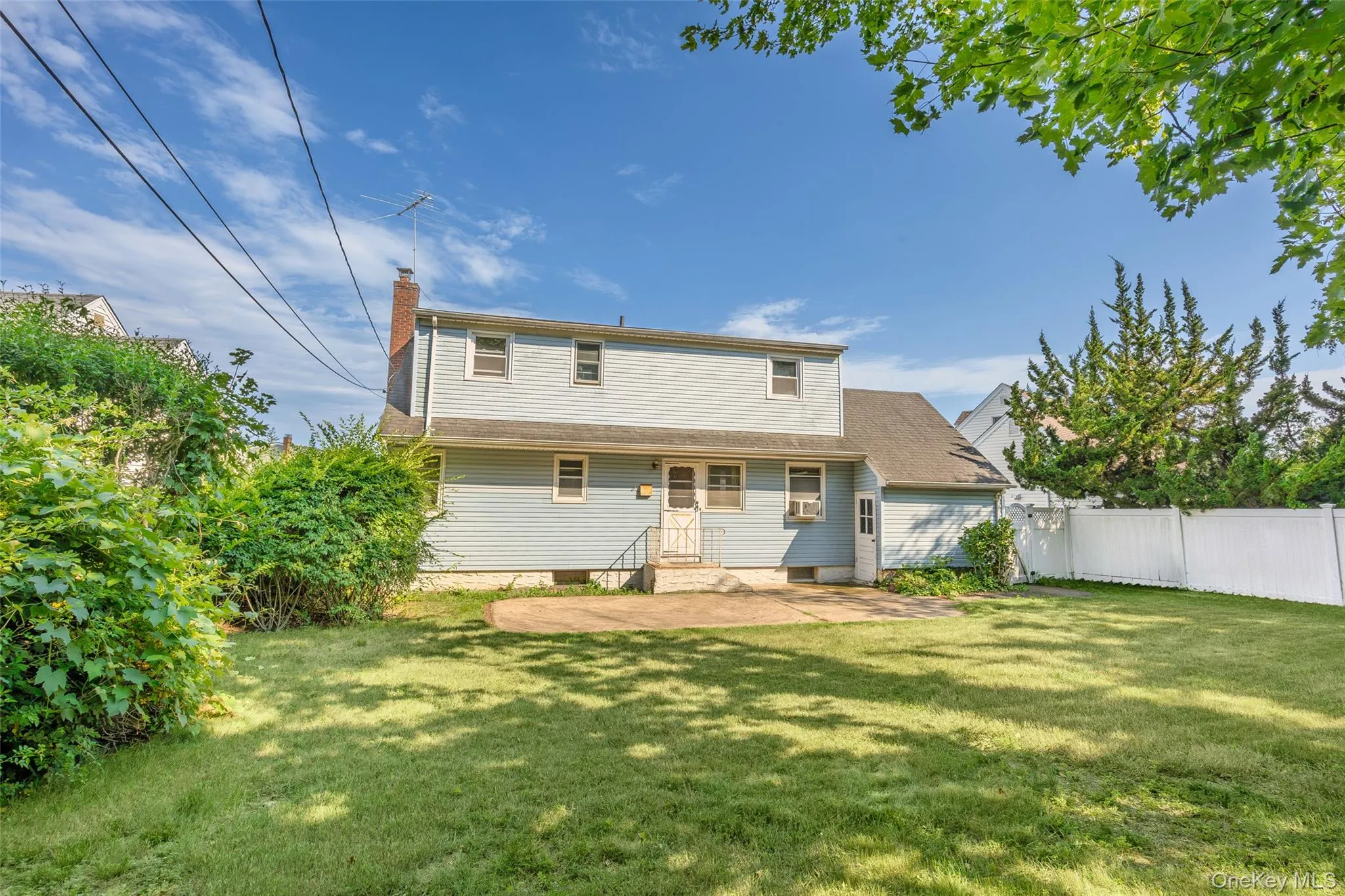 Expansive rear yard featuring a concrete patio, mature perimeter plantings, and a white privacy fence Expansive rear yard featuring a concrete patio, mature perimeter plantings, and a white privacy fence
