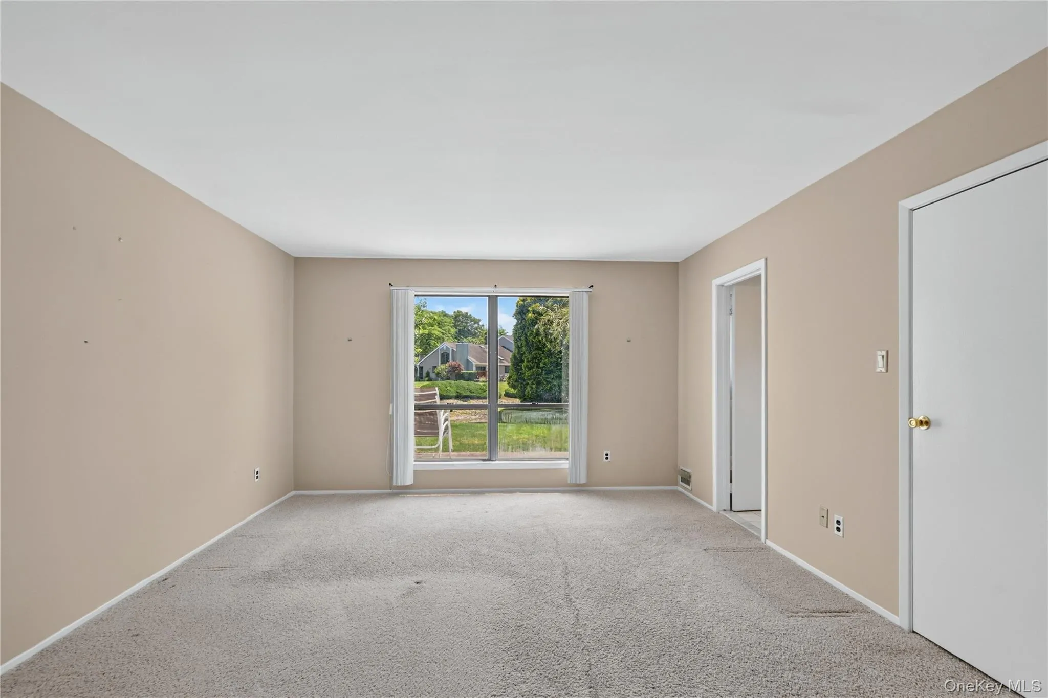 Spacious interior room with neutral-toned walls, light-colored carpeting, and a large window providing outdoor views Spacious interior room with neutral-toned walls, light-colored carpeting, and a large window providing outdoor views