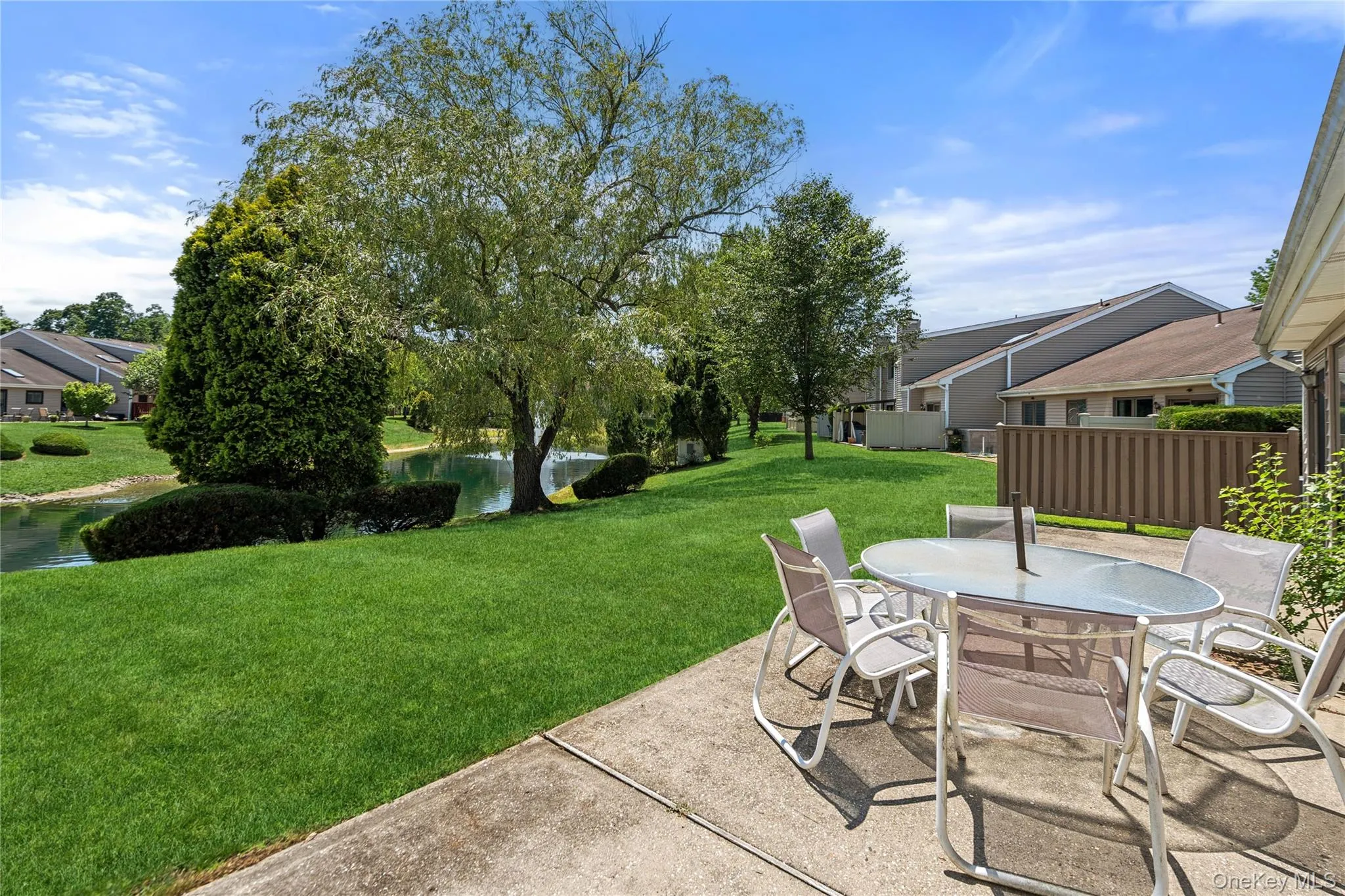 Concrete patio surface bordering a manicured lawn, featuring mature trees and a tranquil pond Concrete patio surface bordering a manicured lawn, featuring mature trees and a tranquil pond