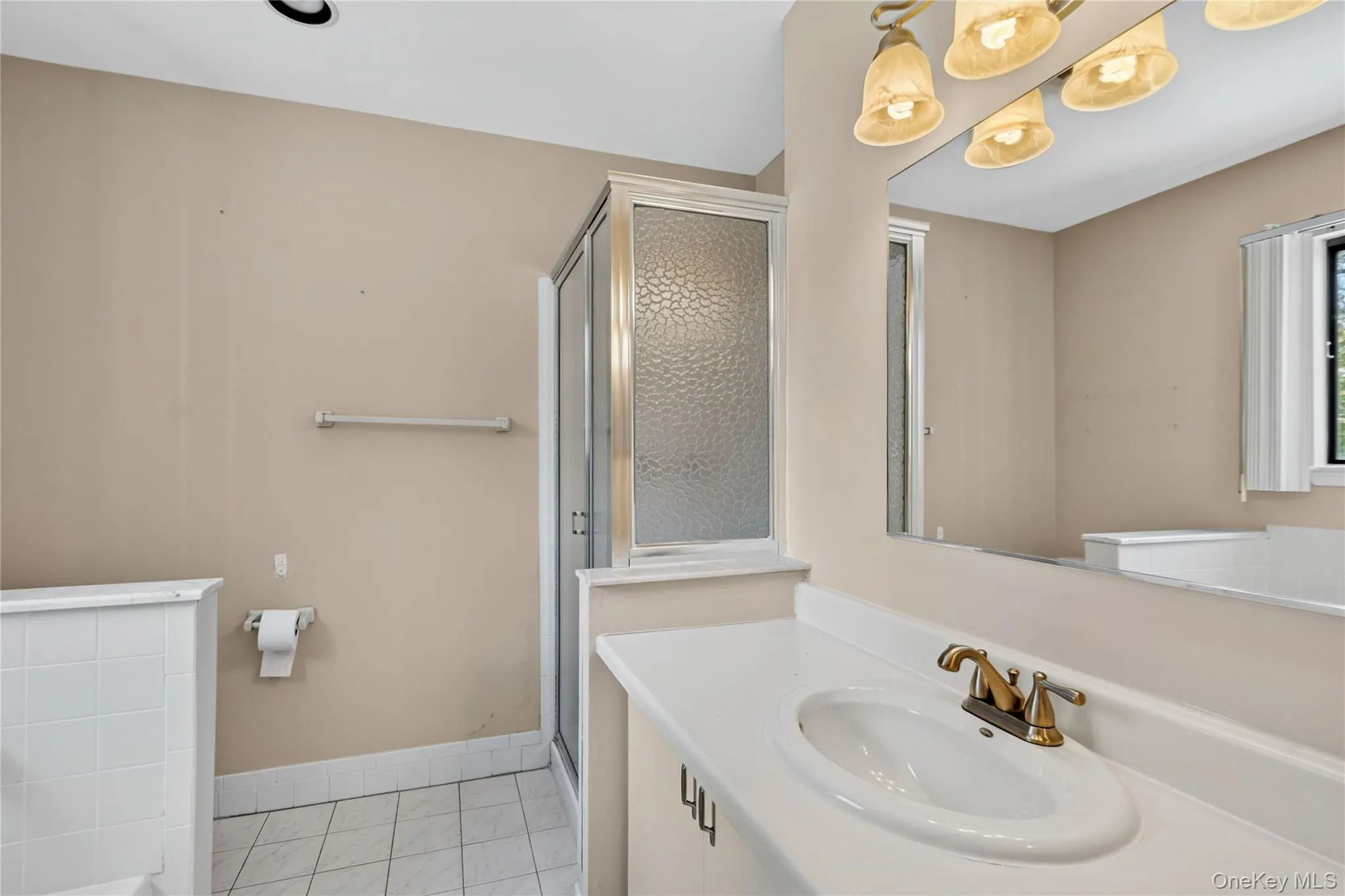 Bathroom vanity featuring a white oval sink with a brass-finish faucet, a large wall-mounted mirror, and a four-light fixture Bathroom vanity featuring a white oval sink with a brass-finish faucet, a large wall-mounted mirror, and a four-light fixture