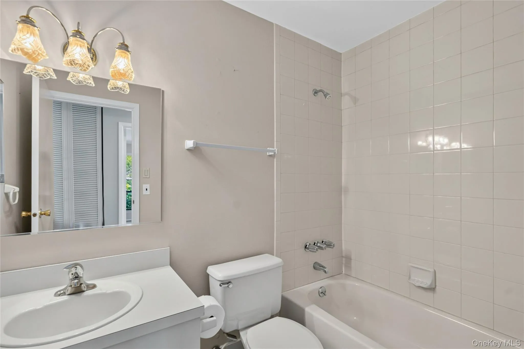 Bathroom featuring a white vanity with an integrated sink, a rectangular mirror, and a three-light fixture with decorative glass shades Bathroom featuring a white vanity with an integrated sink, a rectangular mirror, and a three-light fixture with decorative glass shades