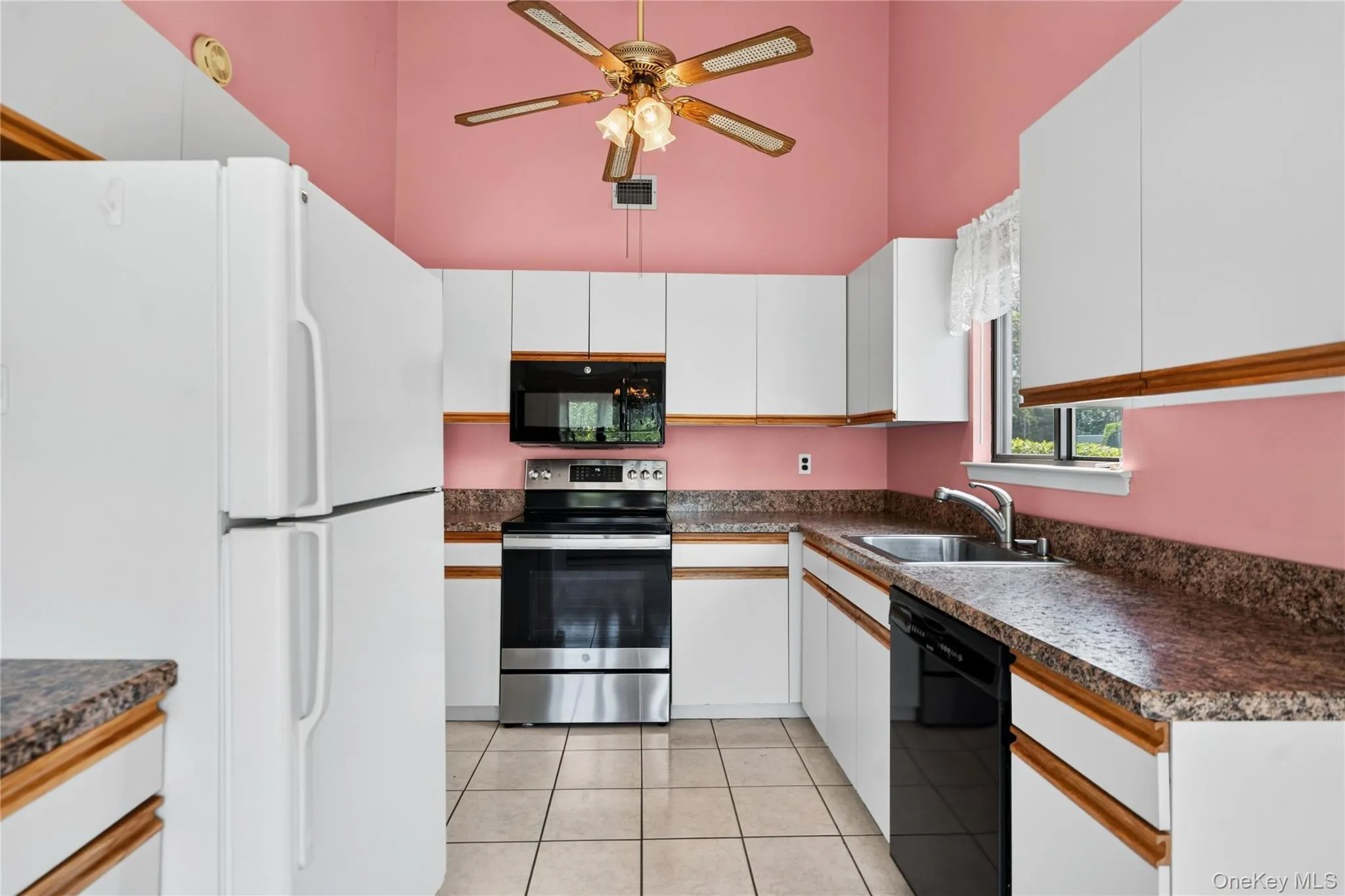 Kitchen featuring vaulted ceilings with a ceiling fan, white cabinetry with wood trim, and a window above the sink Kitchen featuring vaulted ceilings with a ceiling fan, white cabinetry with wood trim, and a window above the sink