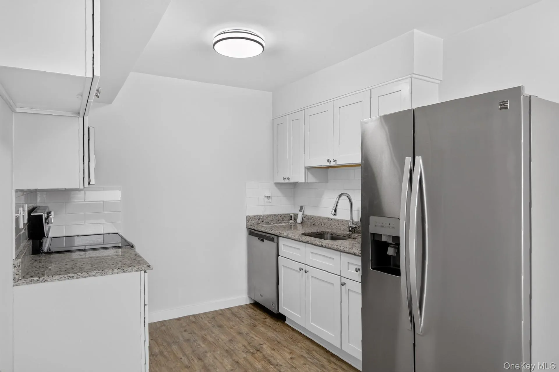Contemporary kitchen featuring white cabinetry, granite-finish countertops, subway tile backsplash, stainless steel appliances, and wood-finish flooring Contemporary kitchen featuring white cabinetry, granite-finish countertops, subway tile backsplash, stainless steel appliances, and wood-finish flooring